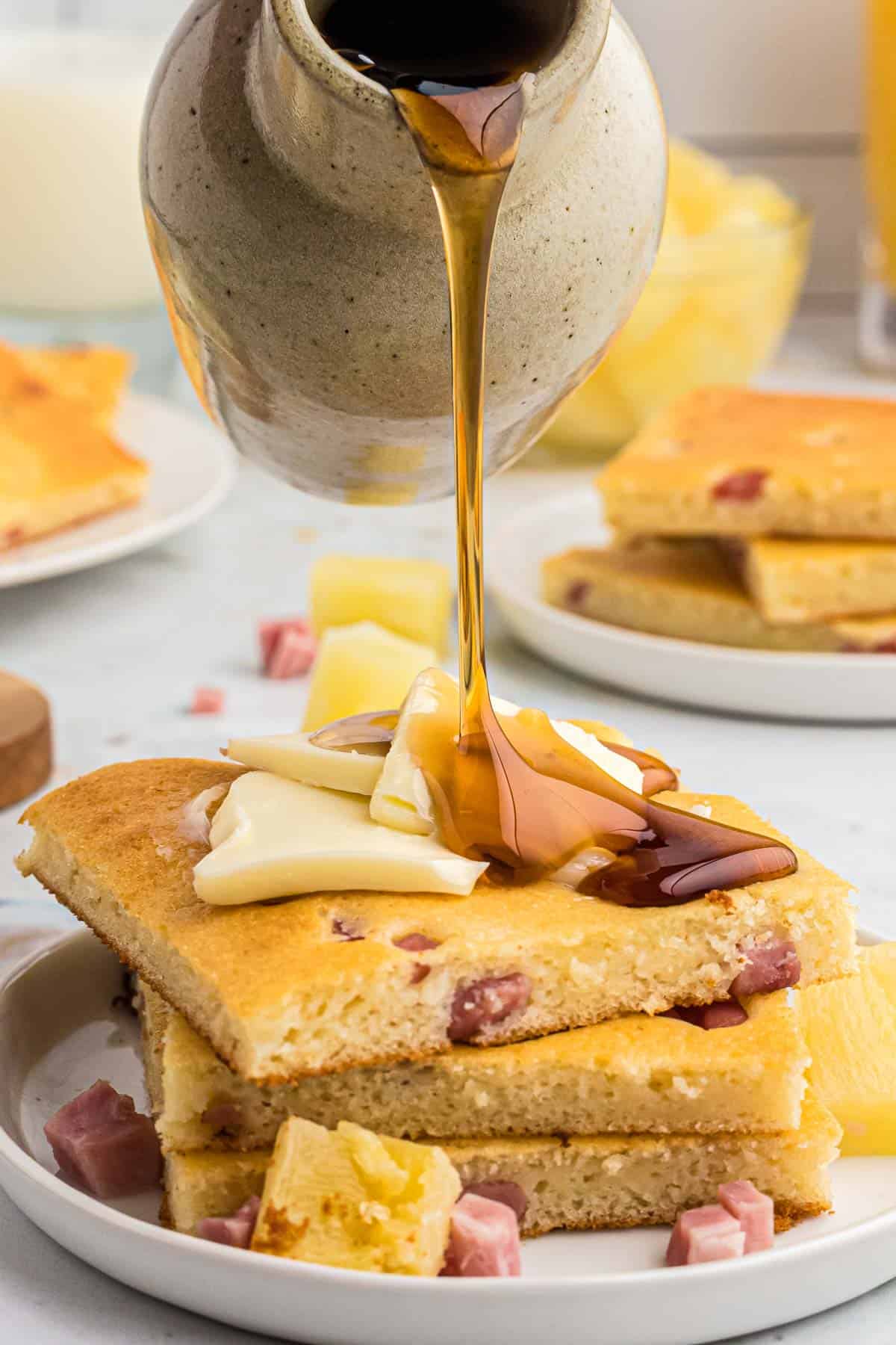 Pile de tranches de pancakes au jambon et à l'ananas, sirop versé sur le dessus.