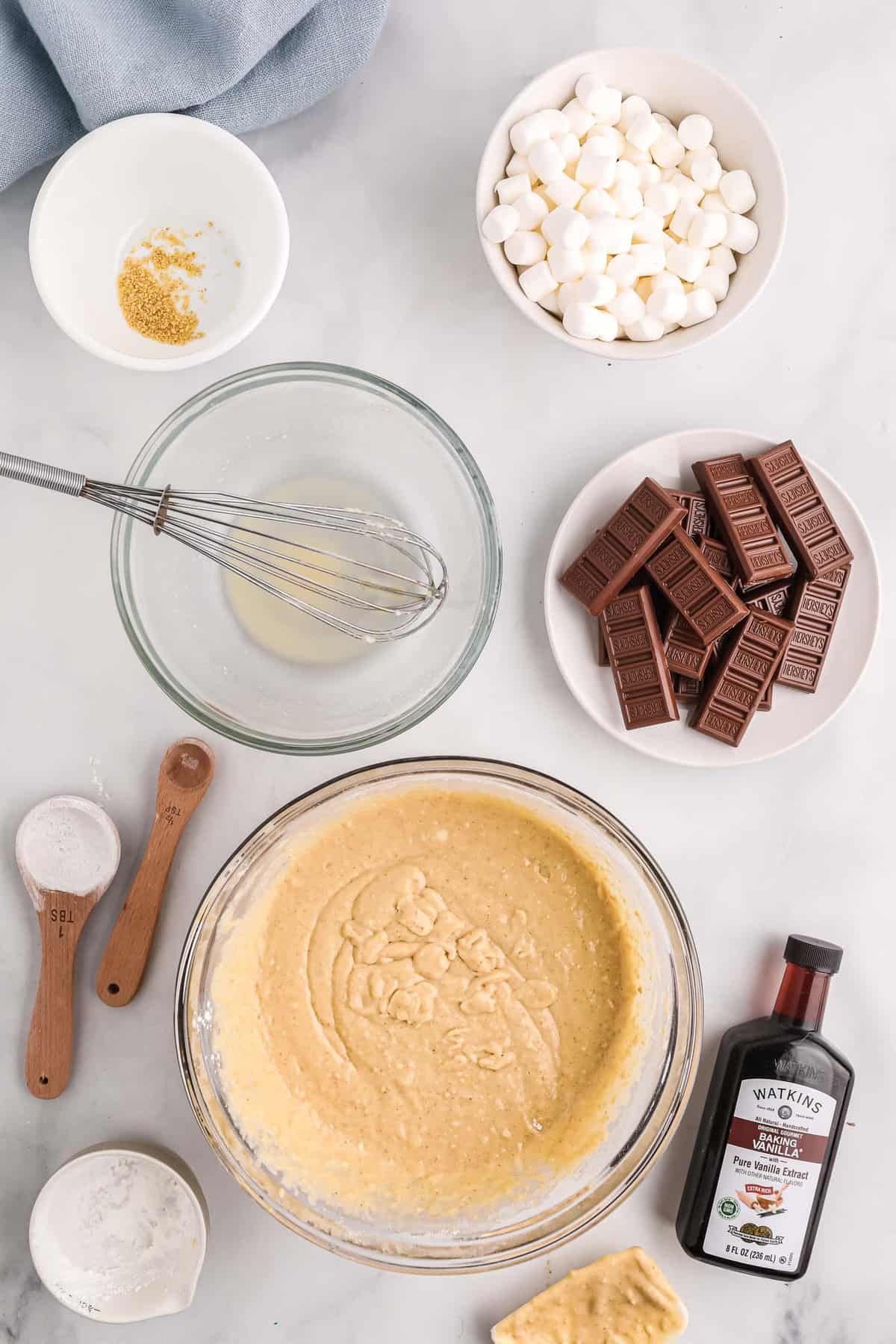 Pâte à pancakes dans un bol. Barres de chocolat et guimauves également visibles.