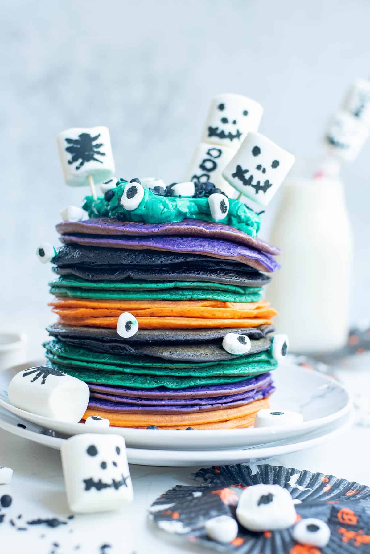 Pancakes verts, orange, violet et noirs empilés, décorés avec des guimauves.
