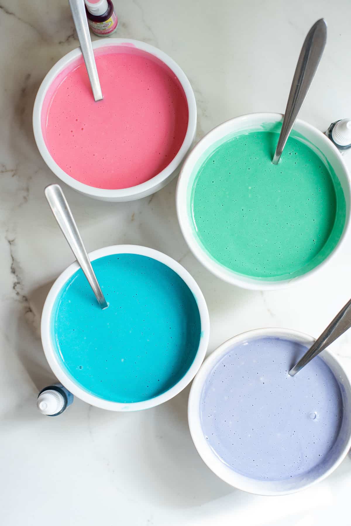 Pâte à pancakes dans quatre bols teints en rose, vert, bleu, violet.