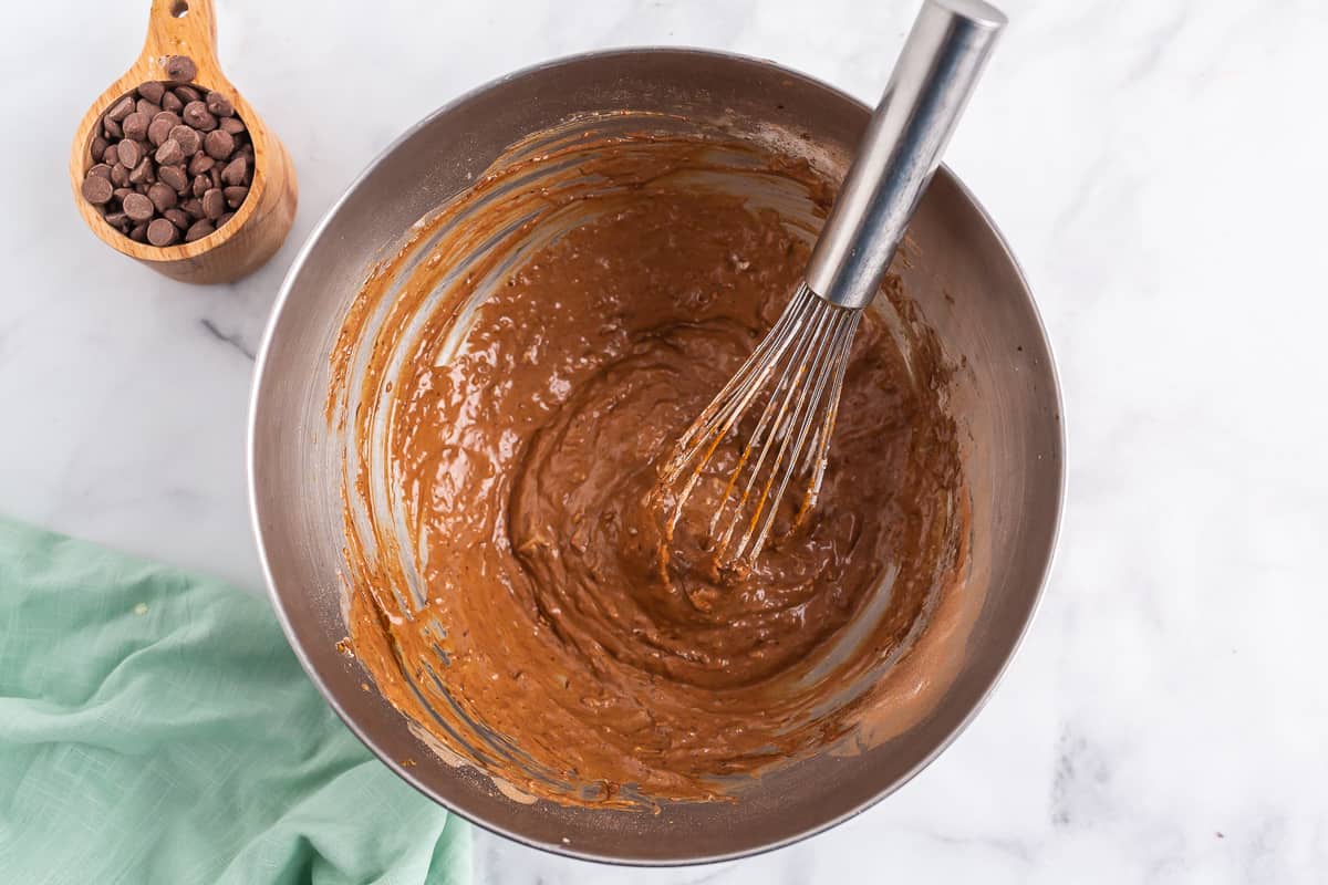 Pâte à pancakes au chocolat et fouet en argent dans un bol en acier inoxydable.
