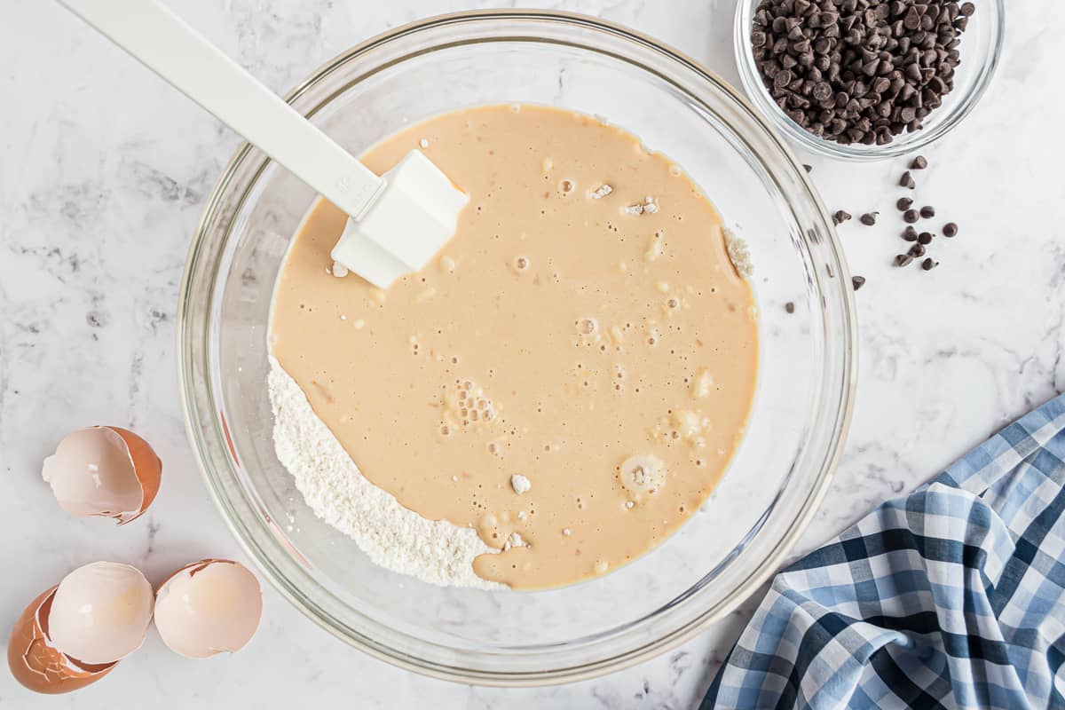 Ingrédients humides et secs mélangés ensemble avec une spatule blanche.