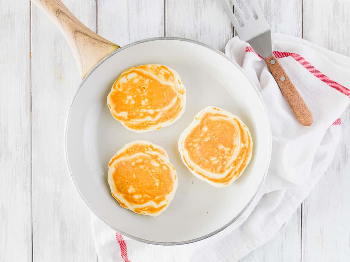 Pancakes cuits dans une poêle blanche.