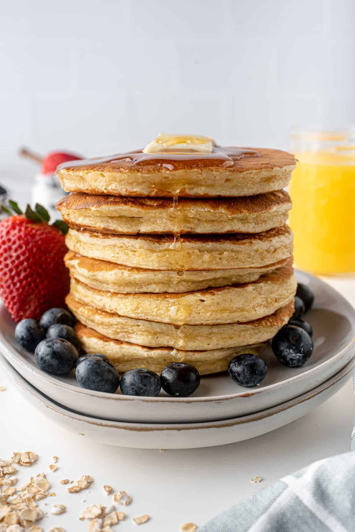 Haute pile de pancakes, entourée de fruits frais, dégoulinant de sirop d'érable.