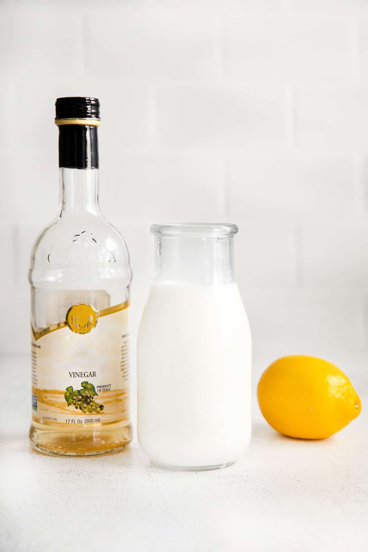 De gauche à droite, une bouteille de vinaigre, un pot de lait, et un citron.