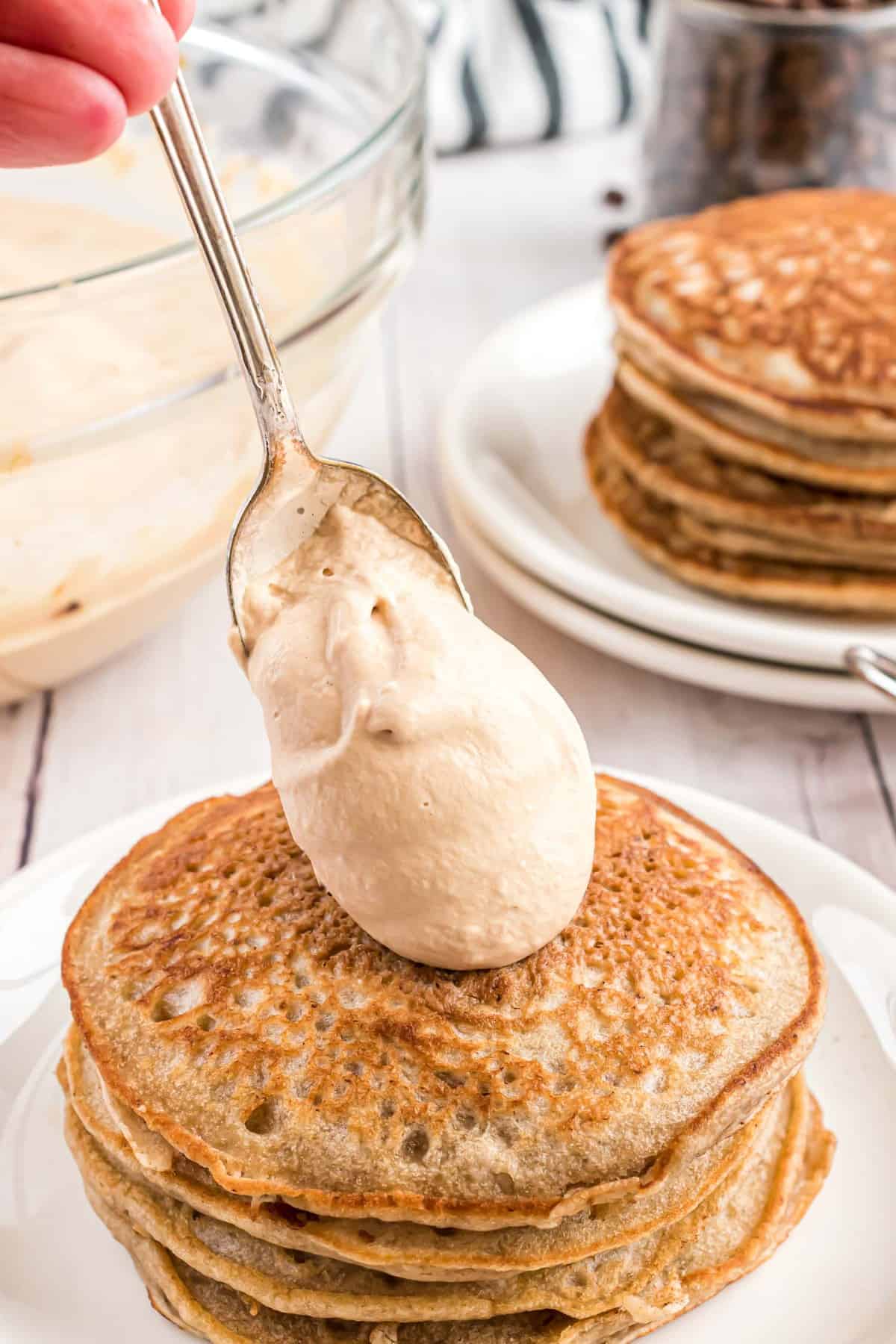 Crème fouettée étant déposée sur une pile de pancakes.