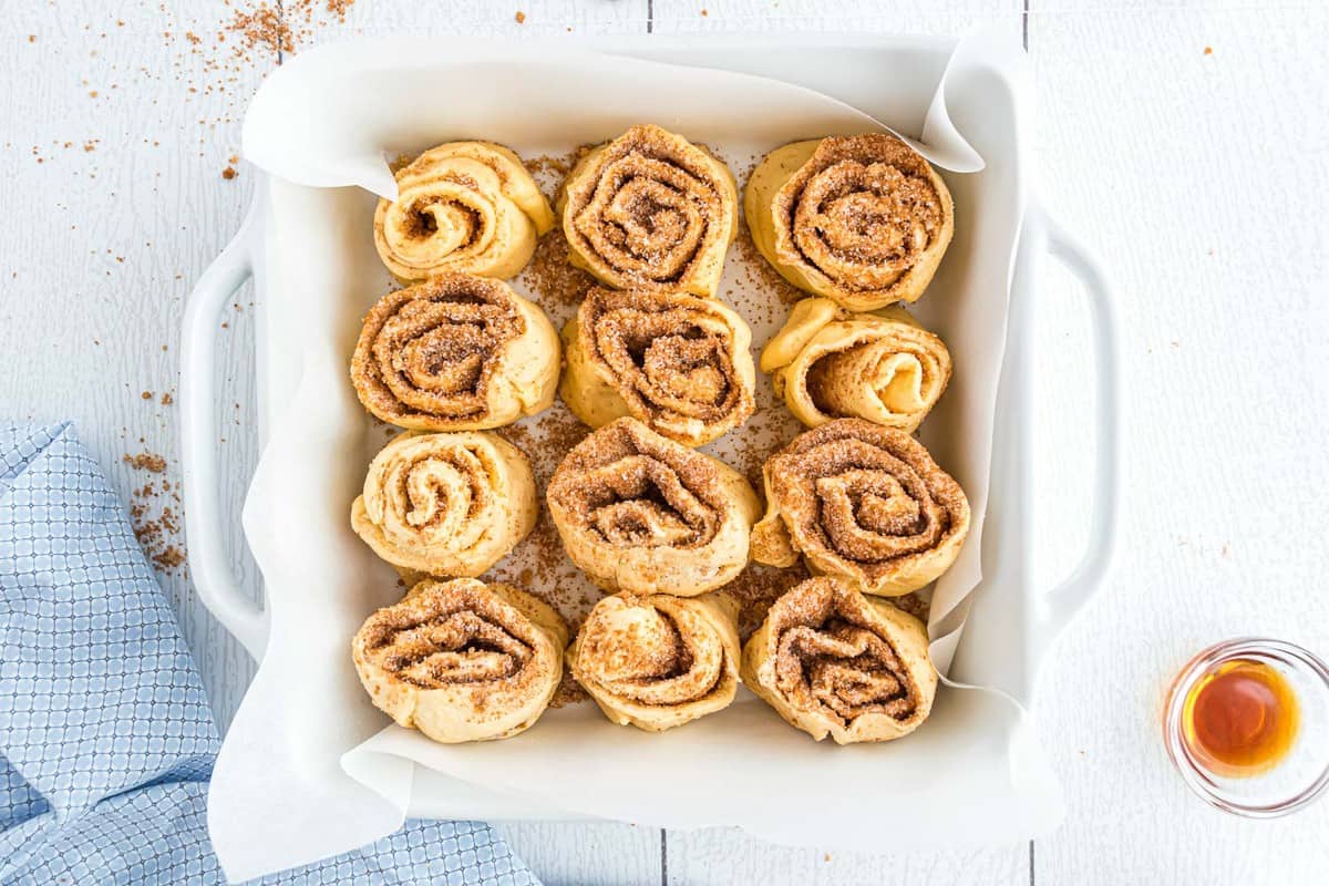 Rouleaux de cannelle non cuits dans un plat de cuisson carré.