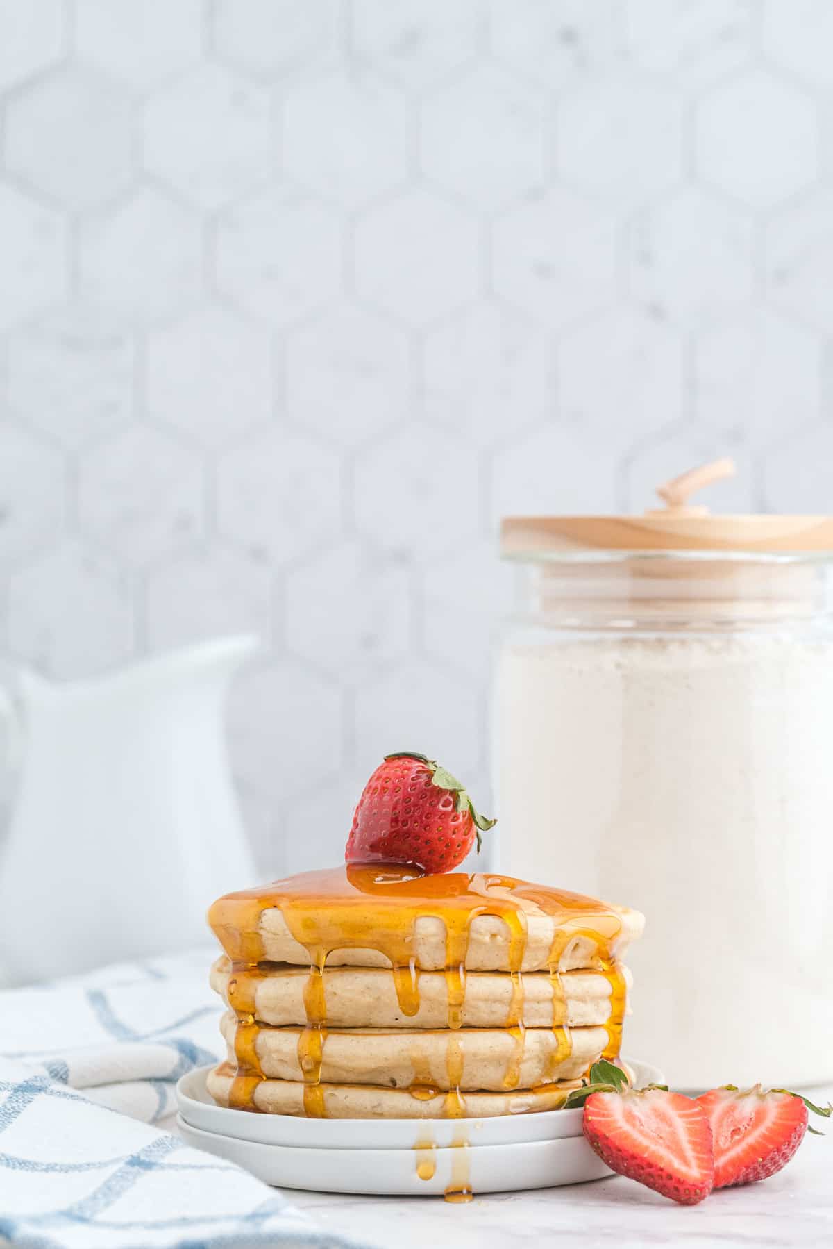 Empilade de pancakes avec du sirop et des fraises, un récipient de mélange à pancakes en arrière-plan.