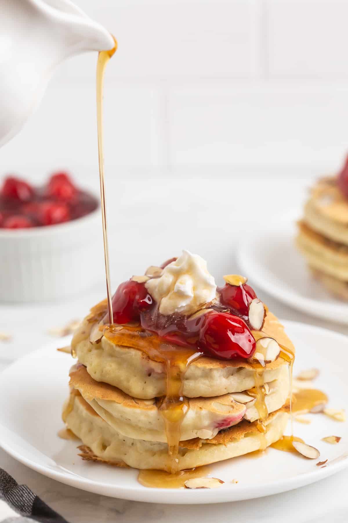 Cerises et crème fouettée sur une pile de pancakes, arrosée de sirop.