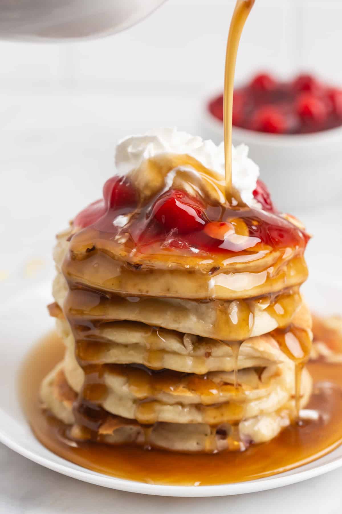 Sirop versé sur une haute pile de pancakes garnis de garniture de tarte aux cerises.