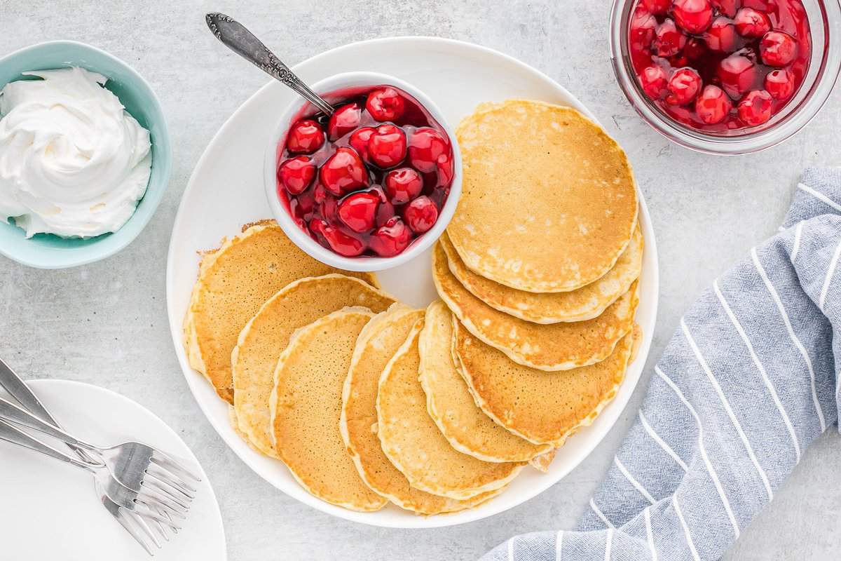 Pancakes sur une assiette ronde avec un petit bol de garniture de tarte aux cerises.