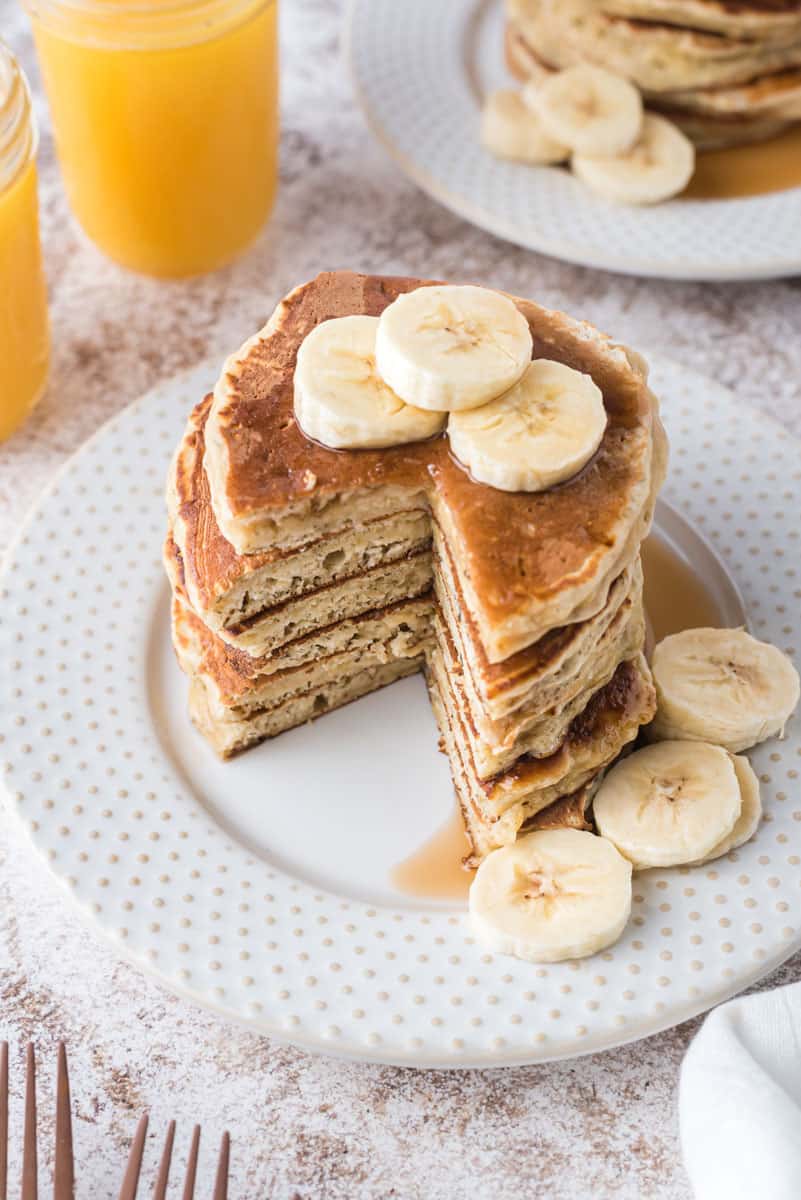 Pile de pancakes garnis de tranches de banane, avec une parts coupée des pancakes.
