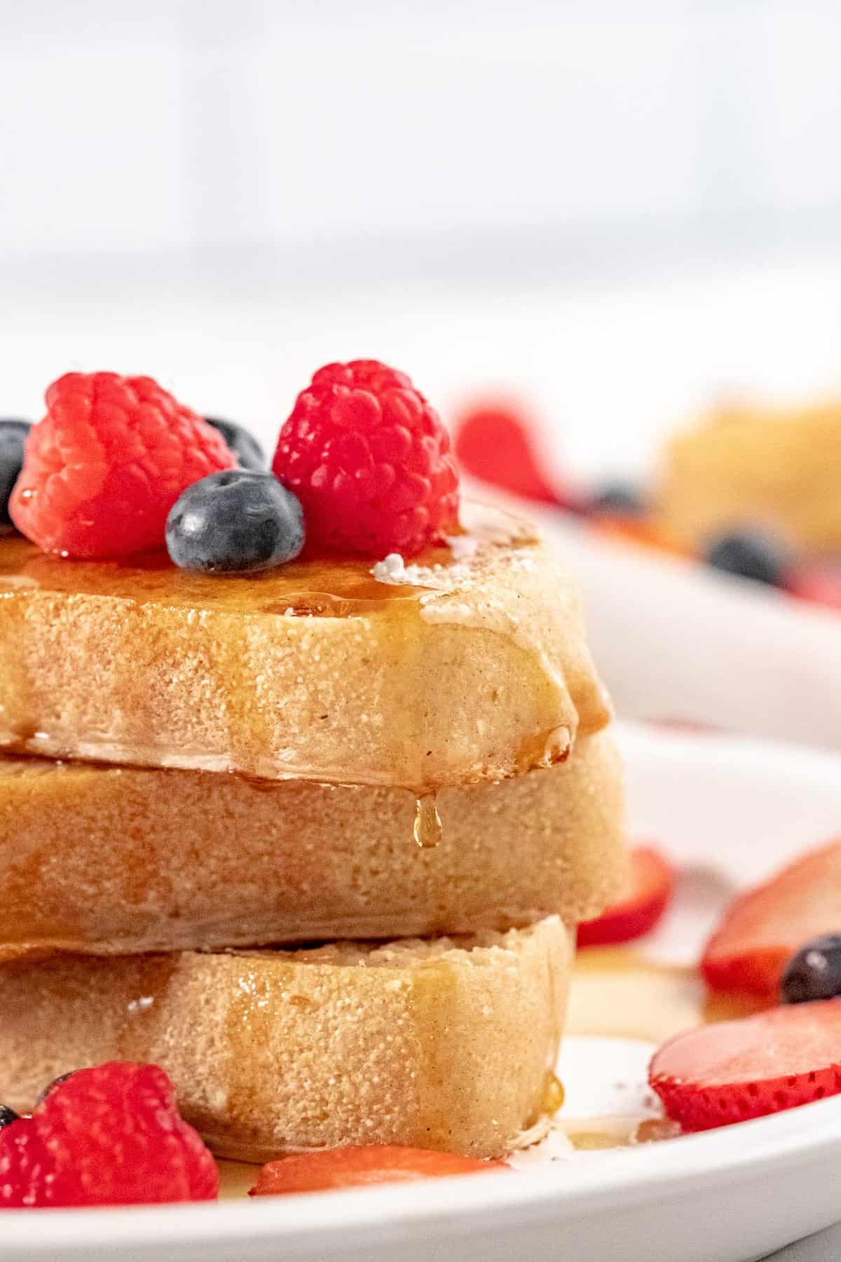 Gros plan sur une pile de trois tranches de pain perdu dégoulinant de sirop.