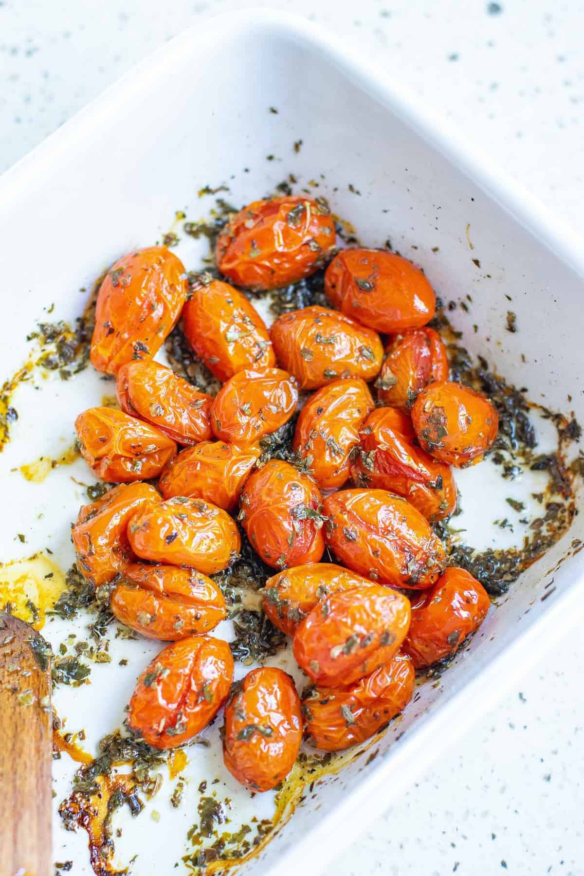 Tomates et assaisonnements dans un plat de cuisson blanc.