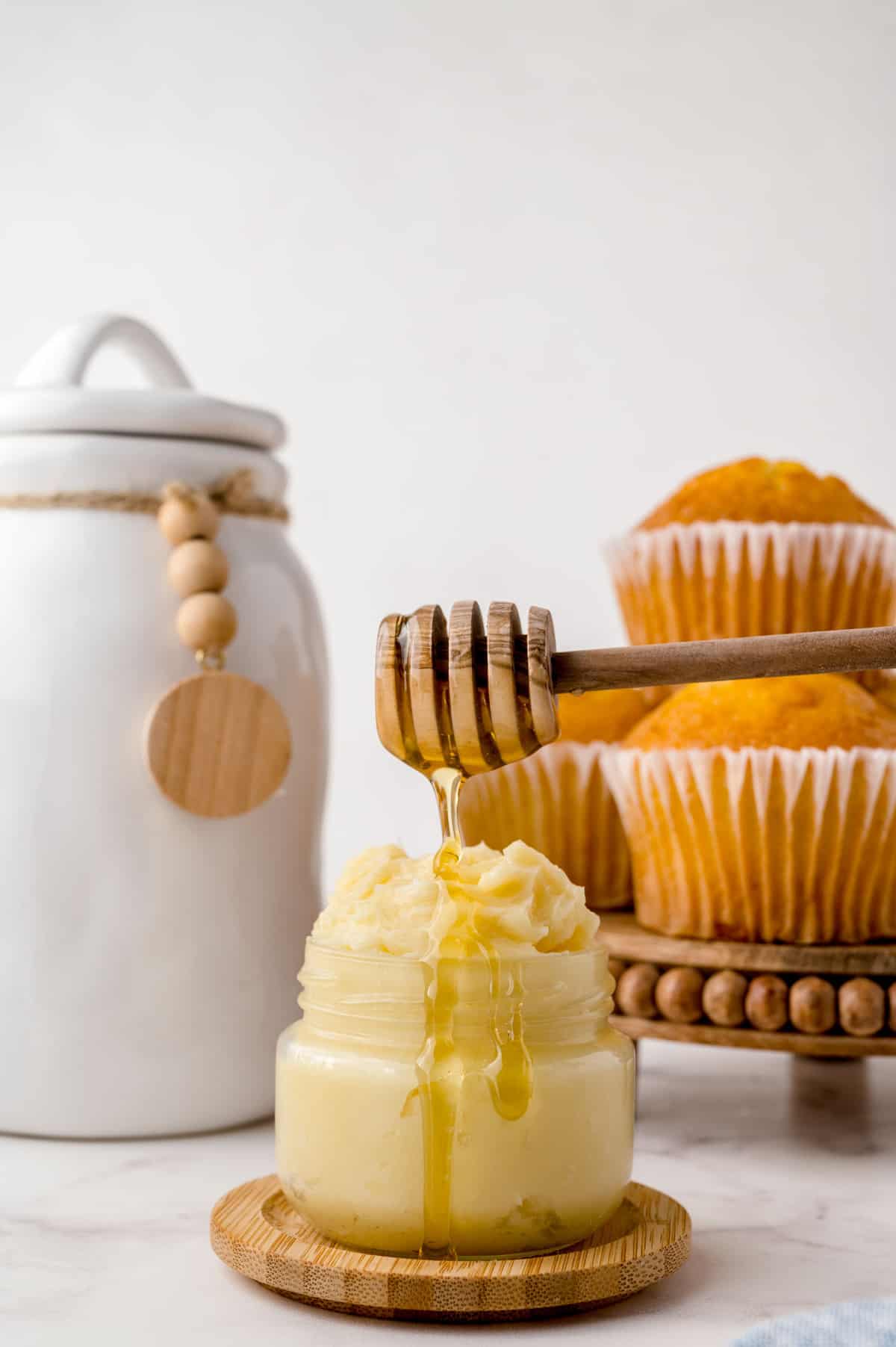 Beurre de miel dans un petit pot avec des muffins de maïs en arrière-plan.