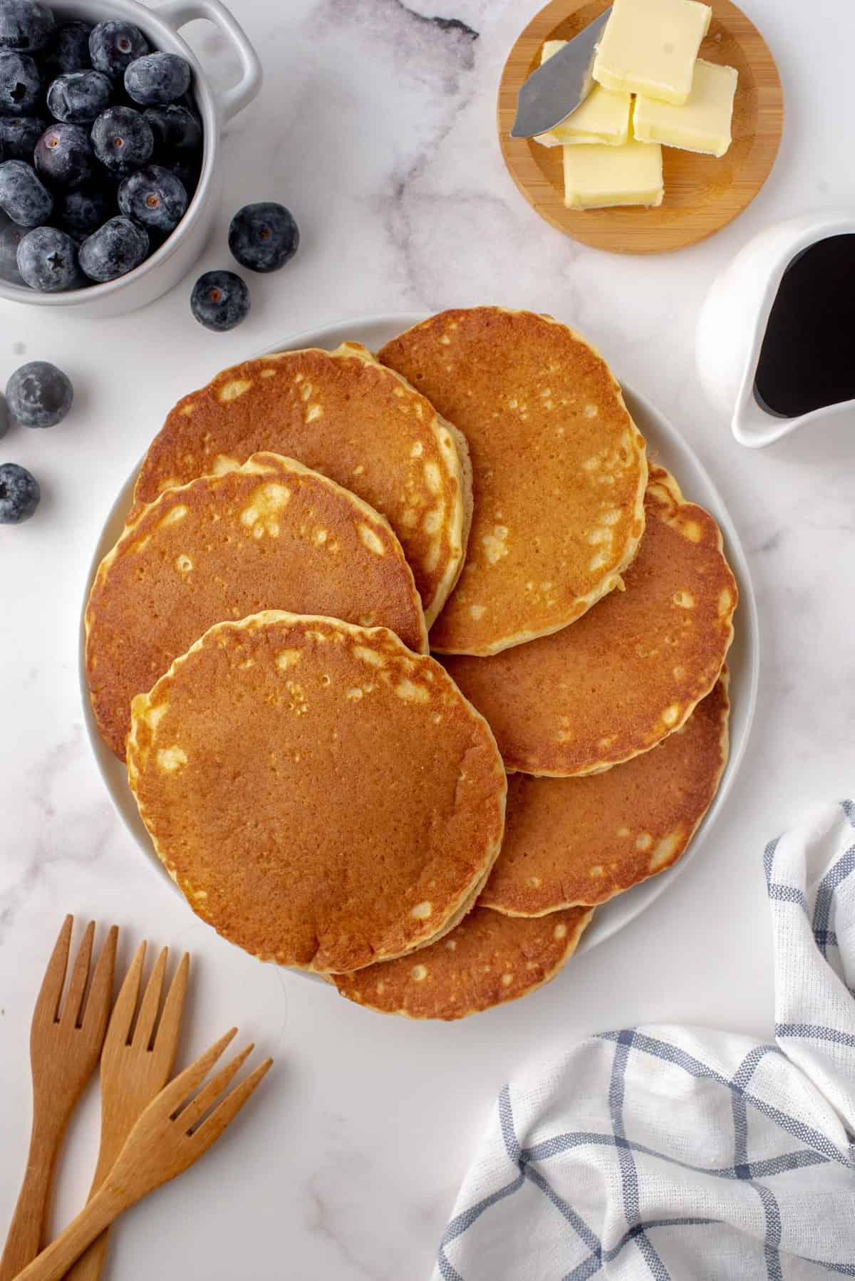Pancakes sur un plateau, beurre et myrtilles à proximité.