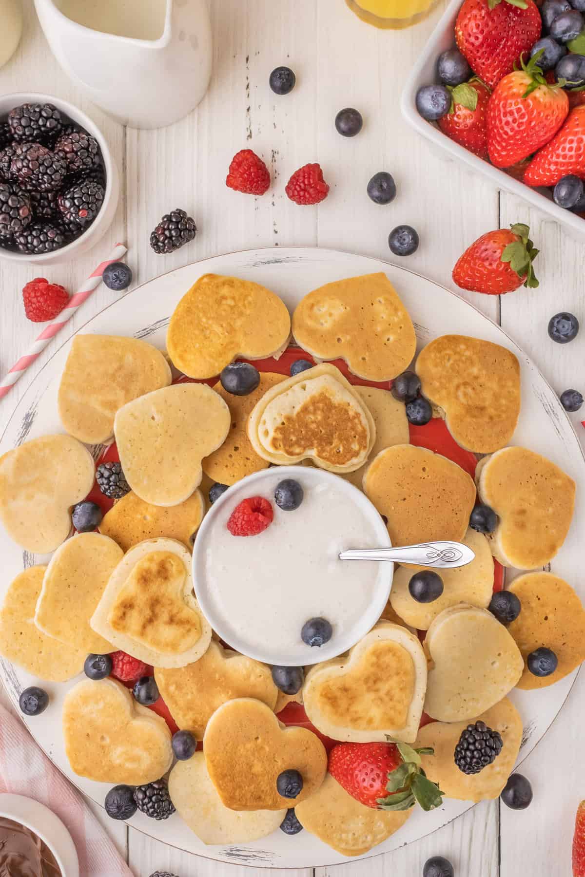 Mini pancakes en forme de cœur sur un plateau avec des fruits.