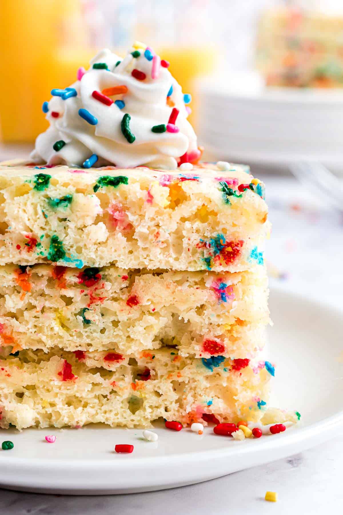 Empilement de pancakes carrés avec des confettis, surmontés de crème fouettée.