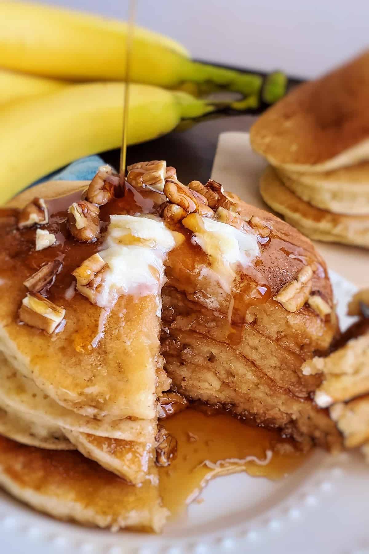 Un sirop versé sur une pile de pancakes garnis de noix et de beurre.