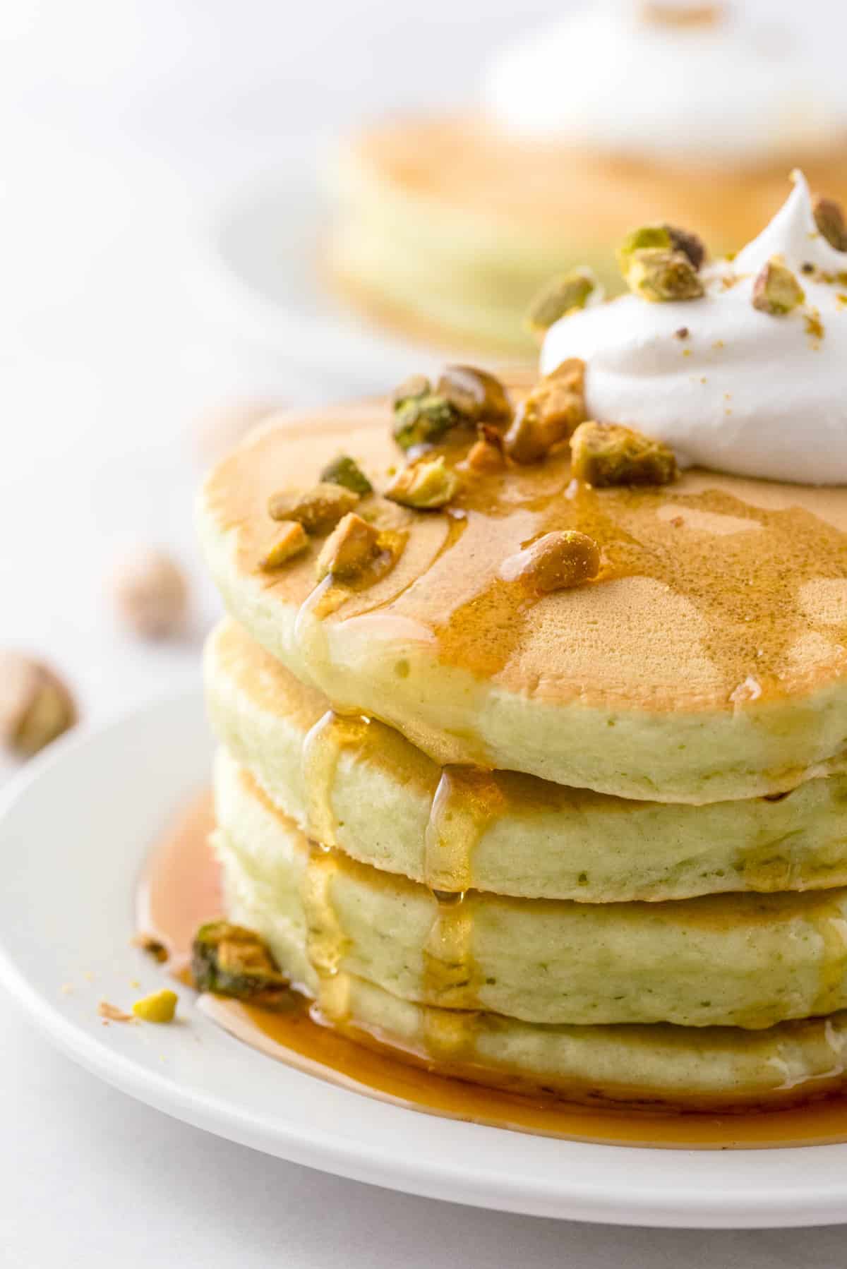 Petite pile de pancakes vert clair, dégoulinant de sirop et garnie de pistaches.