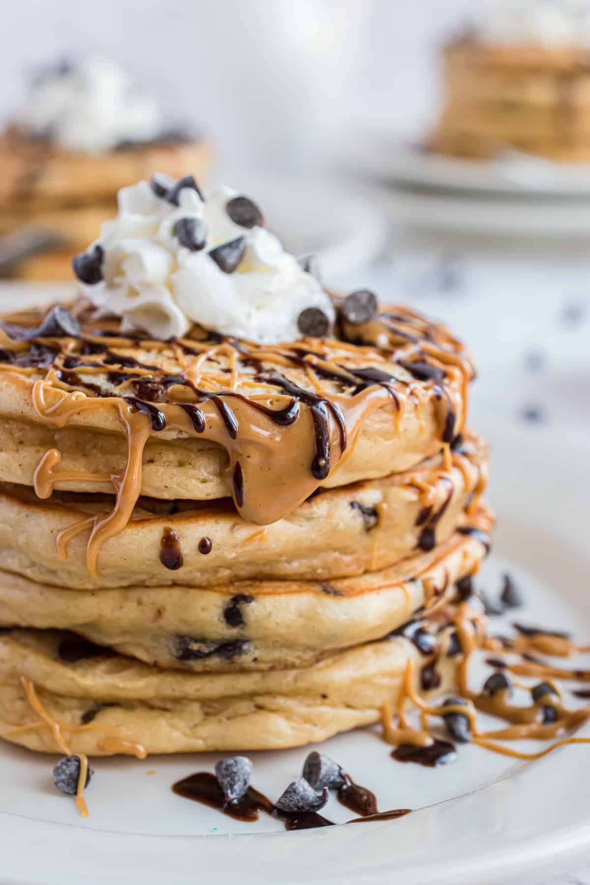Pile de pancakes nappés de beurre de cacahuète et de chocolat, garnis de crème fouettée.