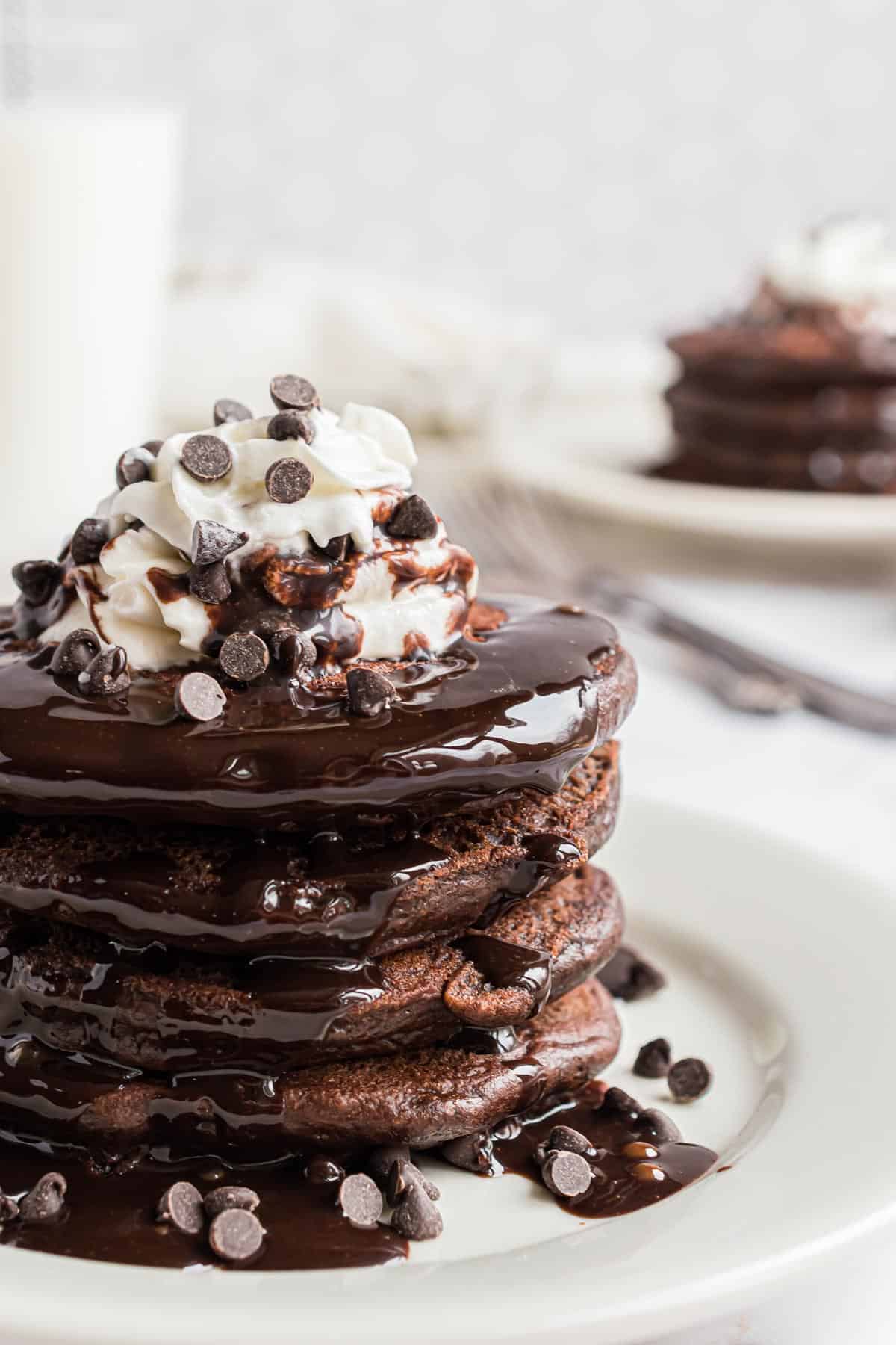 Pile de pancakes au chocolat garnie de crème fouettée, de pépites de chocolat et de sirop chocolat.