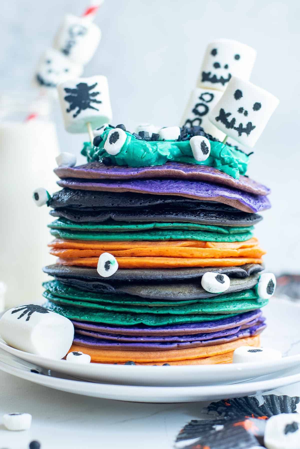 Pile de pancakes multicolores d'Halloween avec des guimauves décorées.