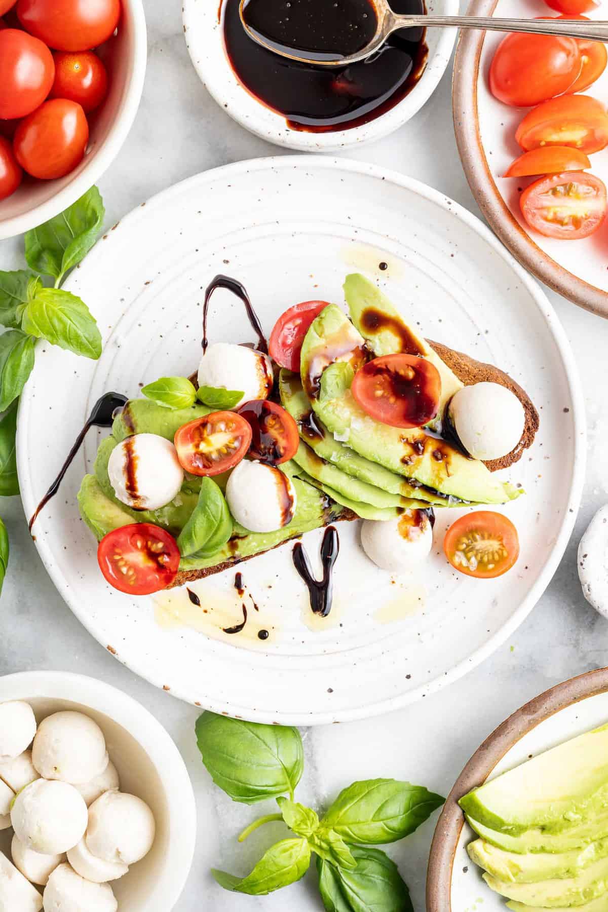 Toast à l'avocat garni de tomates et de mozzarella, entouré d'ingrédients supplémentaires.