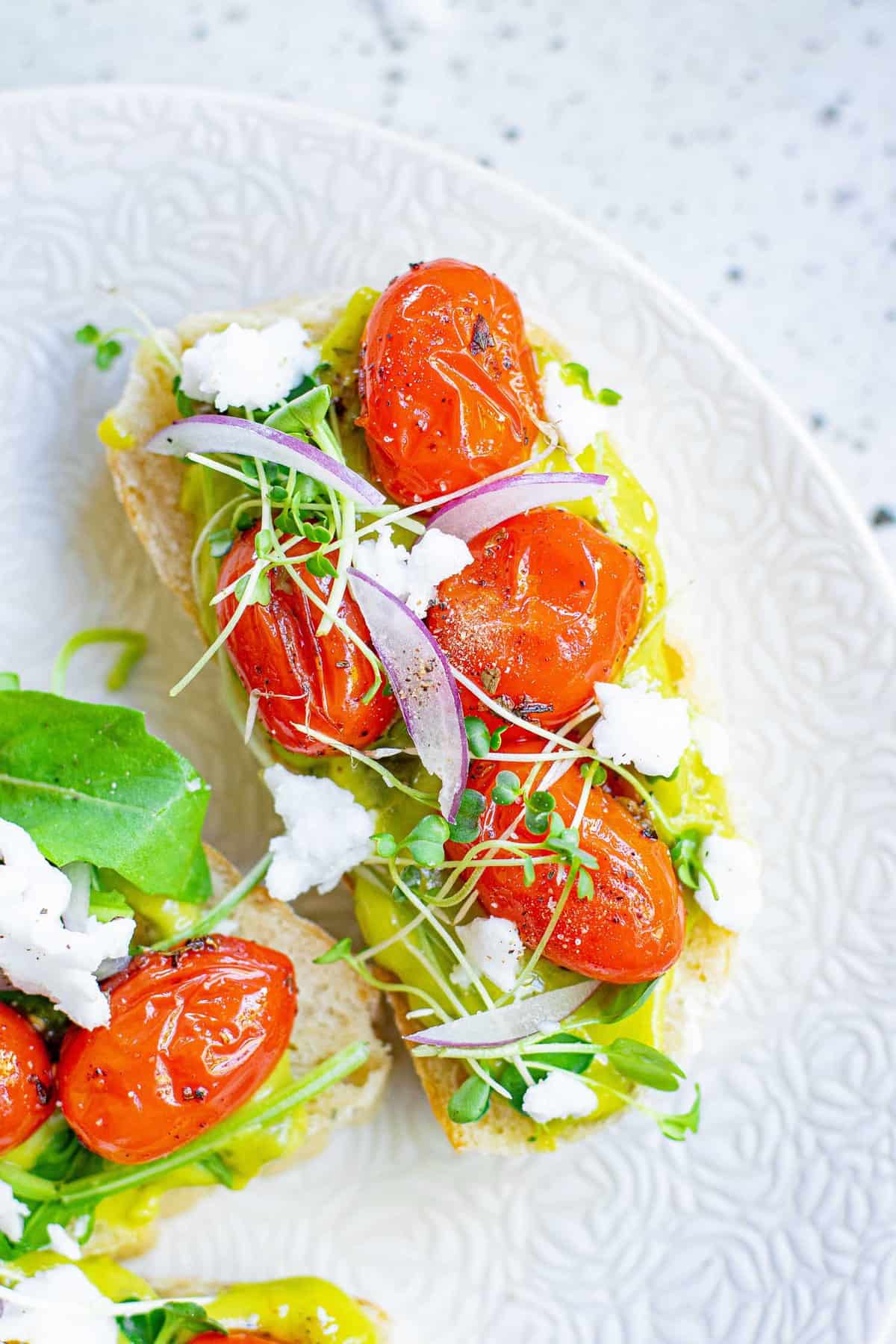 Vue aérienne d'un petit morceau de pain garni de guacamole, de tomates rôties, de légumes et de feta.