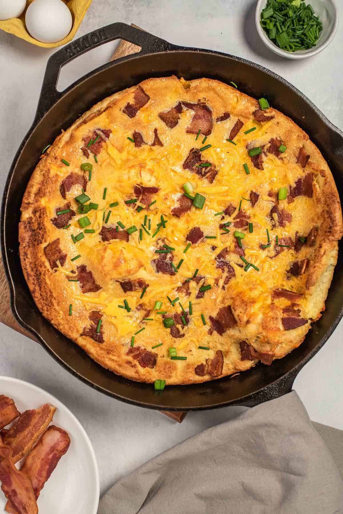 Pancake Dutch baby garni de bacon et de fromage, dans une poêle noire.