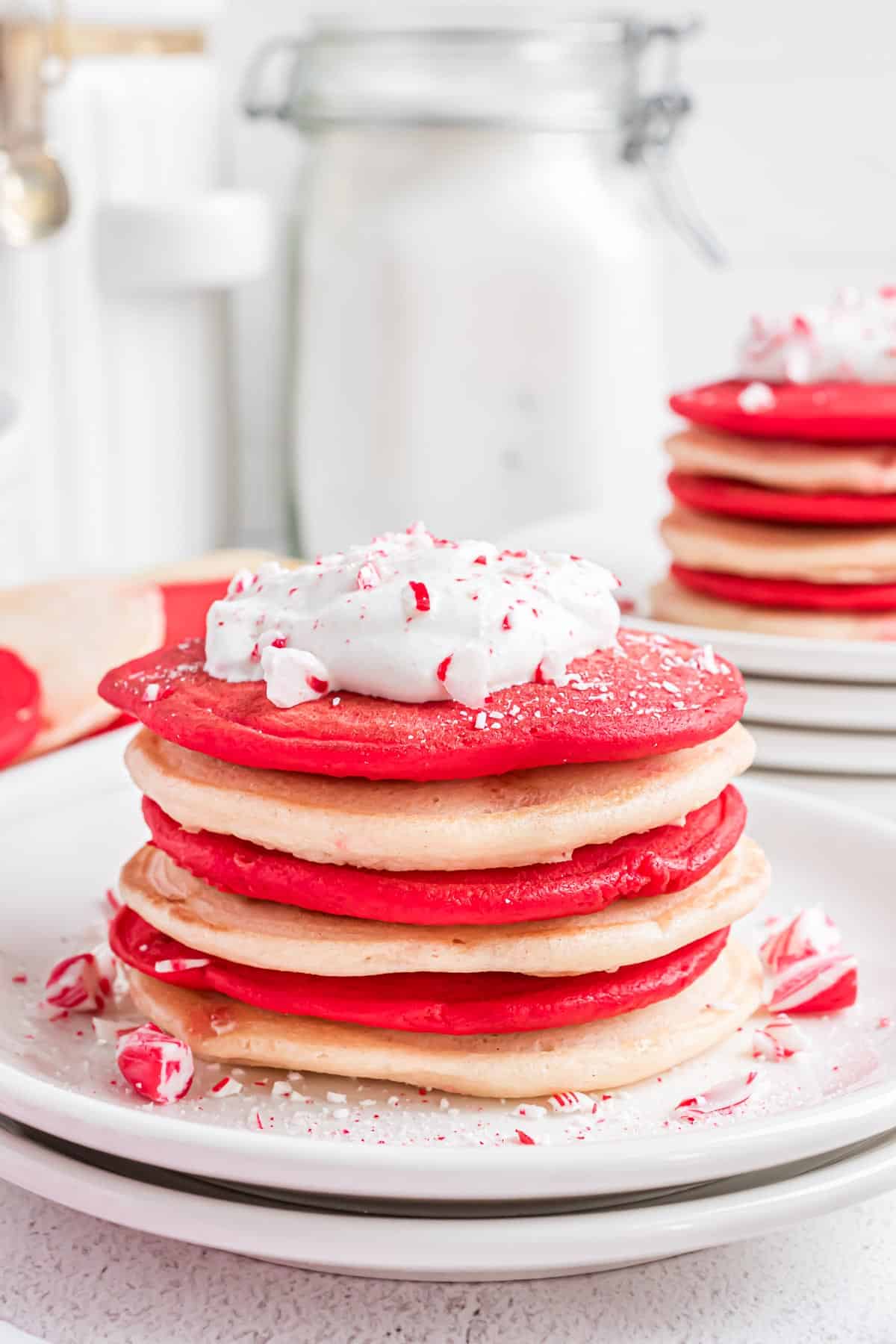 Pancakes rouges et blancs empilés, garnis de crème fouettée et de canne en sucre écrasée.