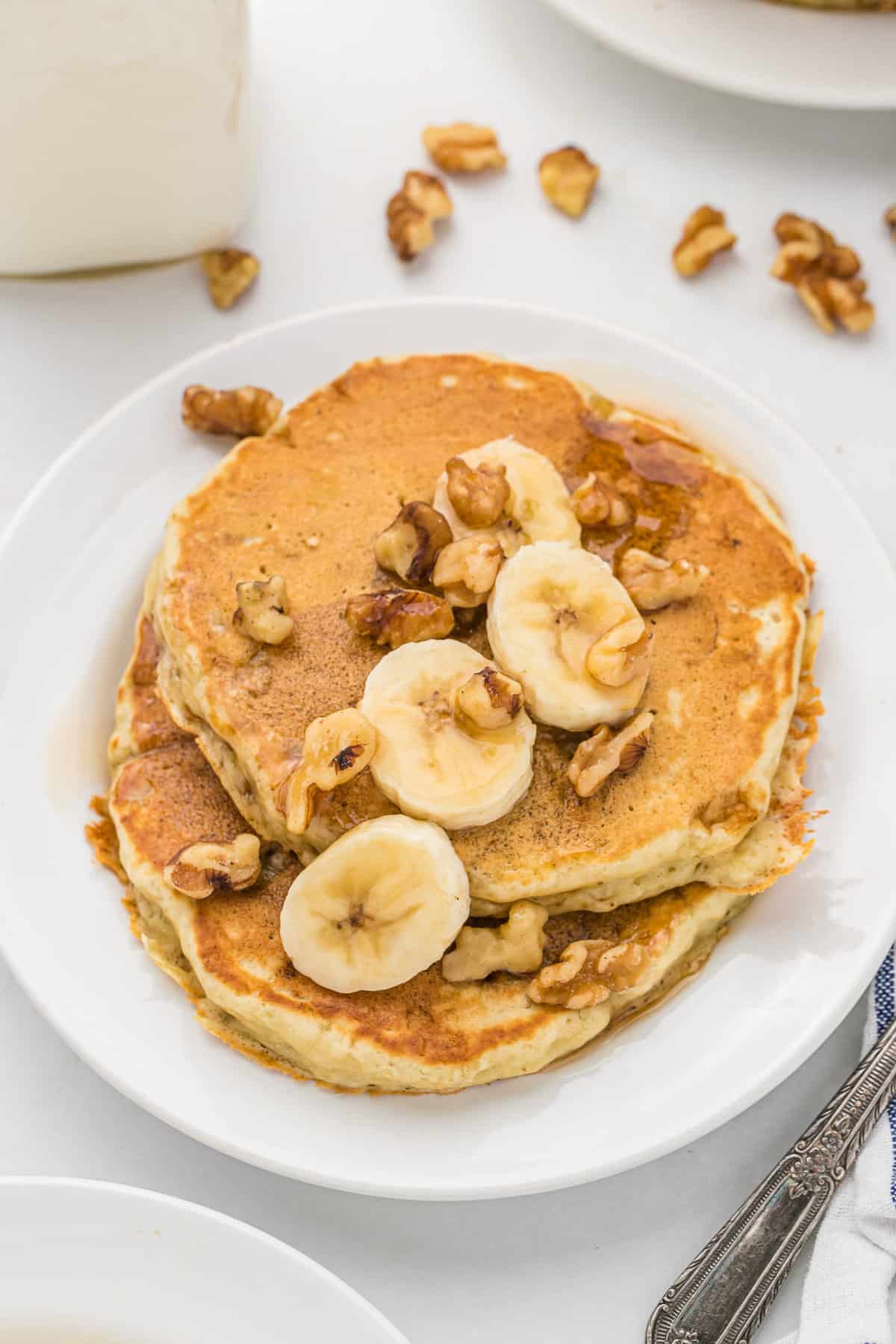 Pancakes à la banane et aux noix sur une assiette blanche.