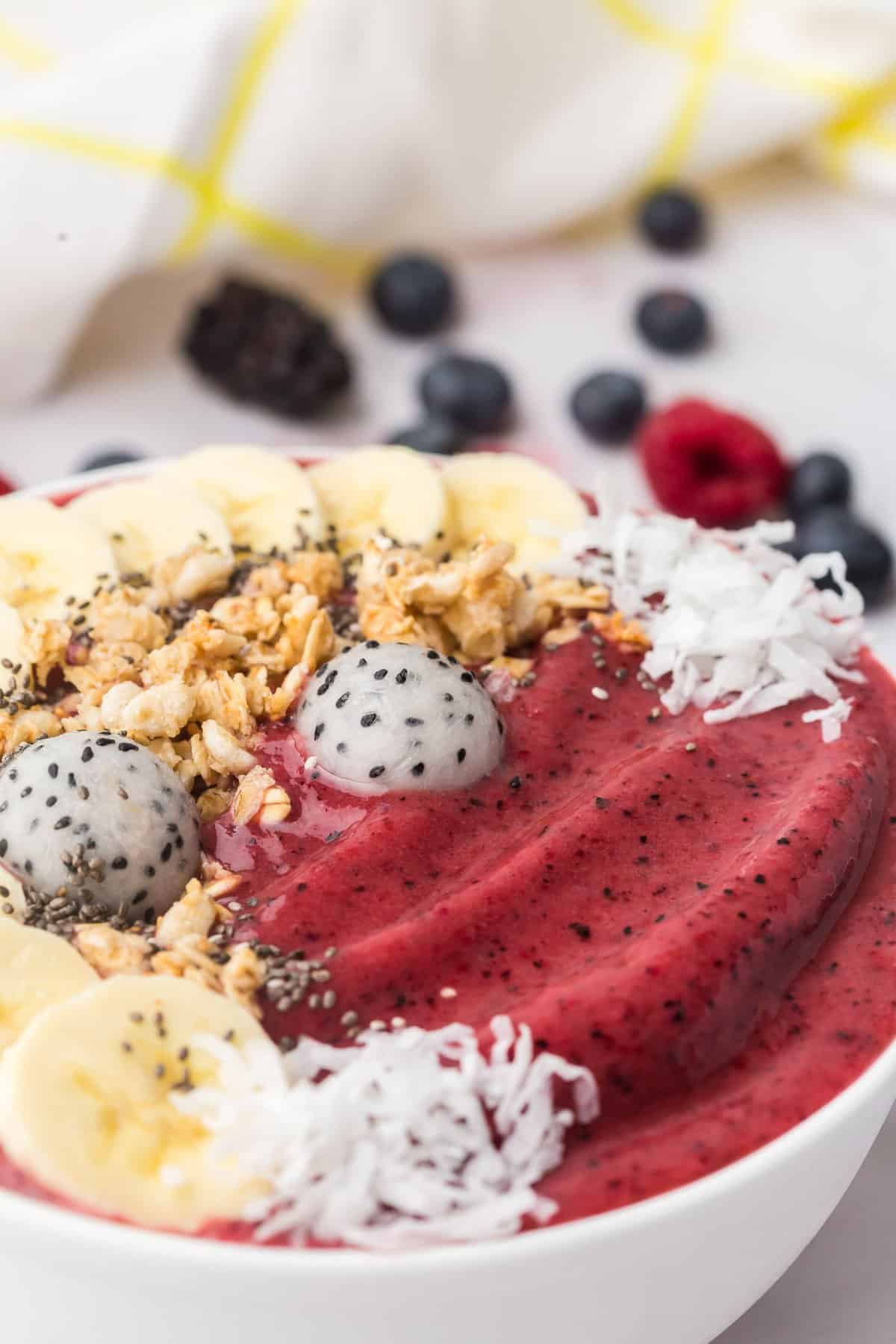 Bol de smoothie rouge foncé garni de fruit du dragon, noix de coco, bananes, graines de chia.
