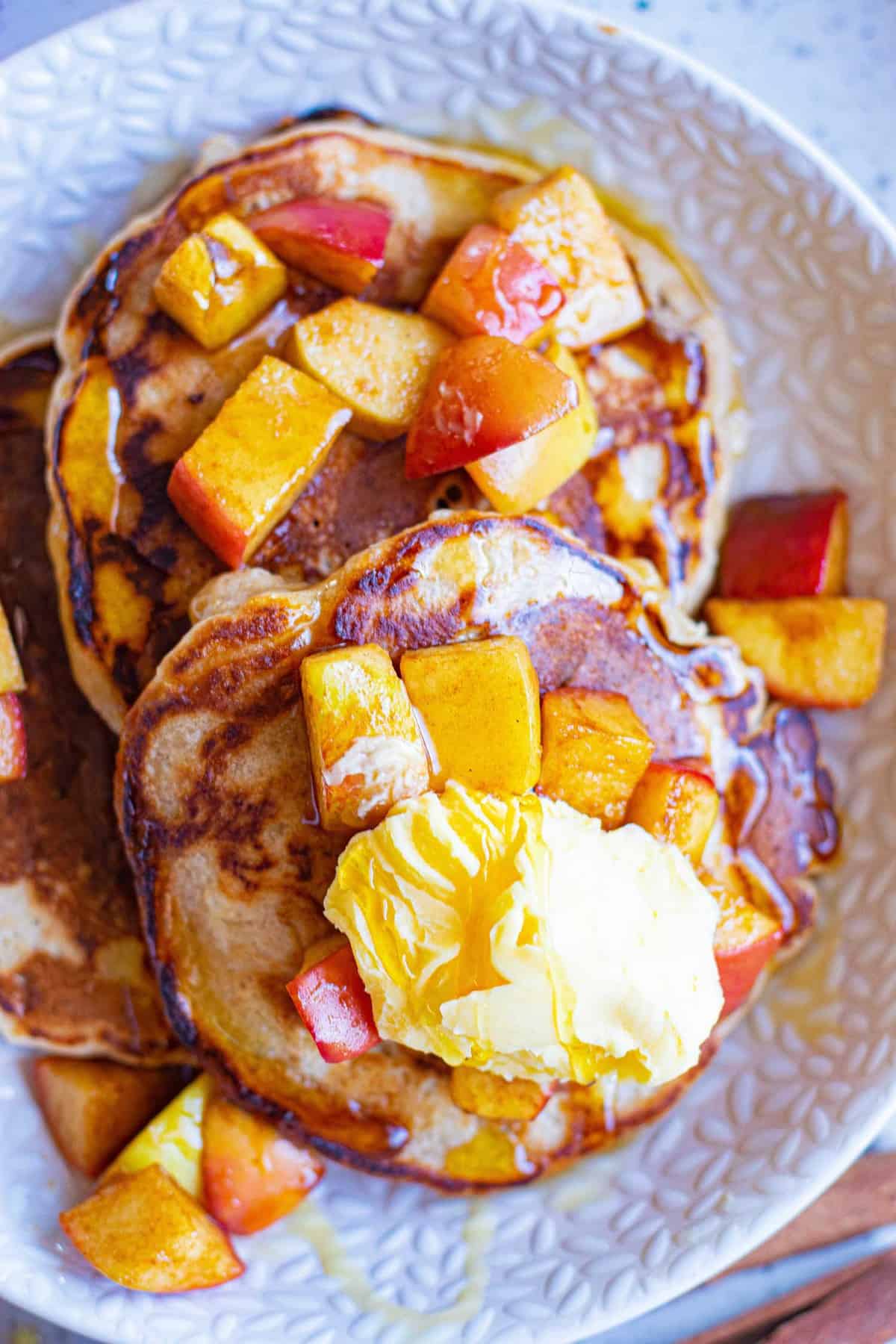 Deux pancakes dans une assiette garnis de beurre et de pommes sautées.