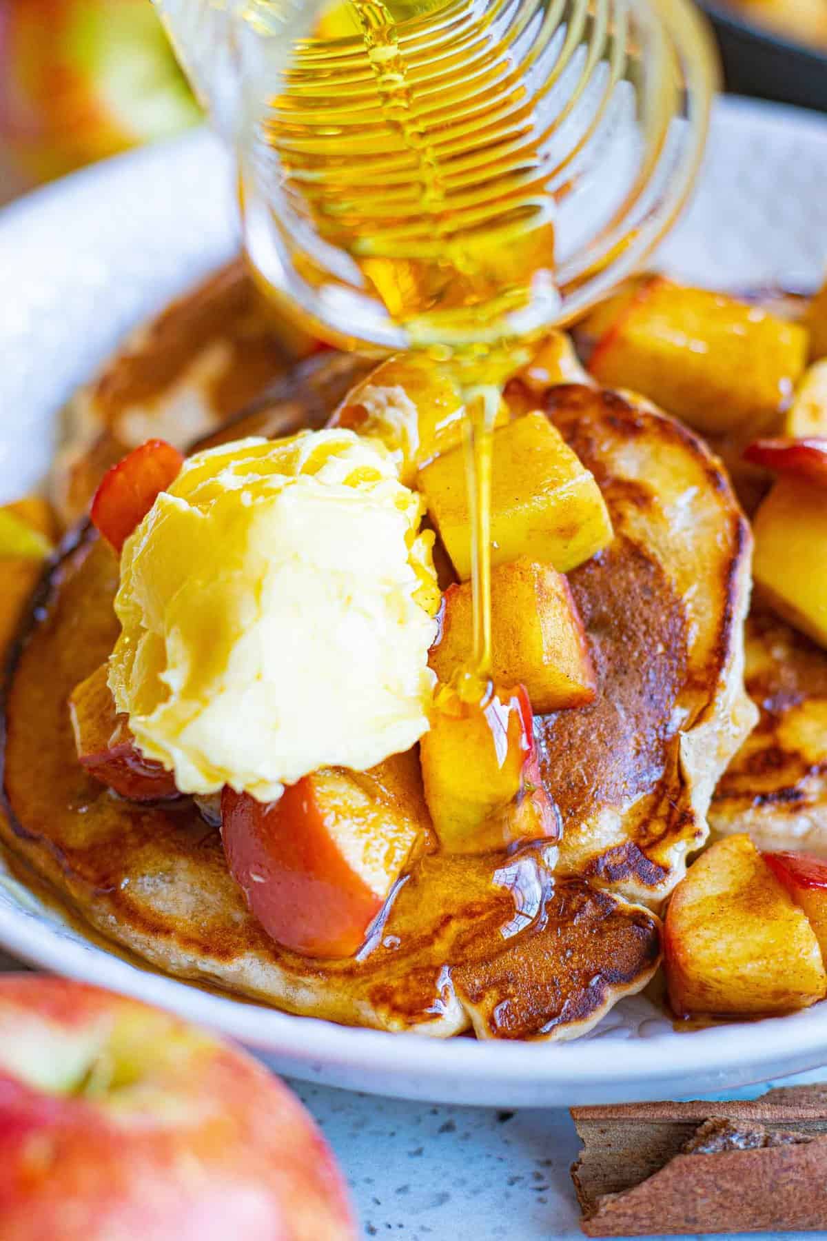 Du sirop versé sur des pancakes garnis de pommes.