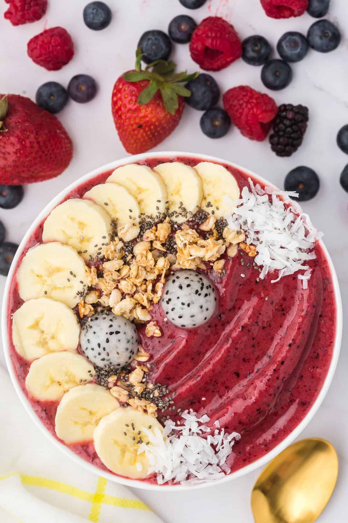 Bol de smoothie aux baies garni de bananes, granola, noix de coco.