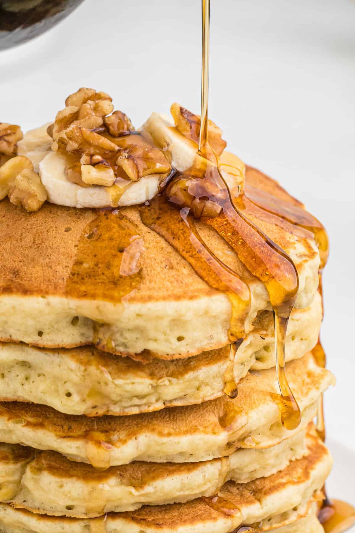 Du sirop versé sur des pancakes à la banane et aux noix.