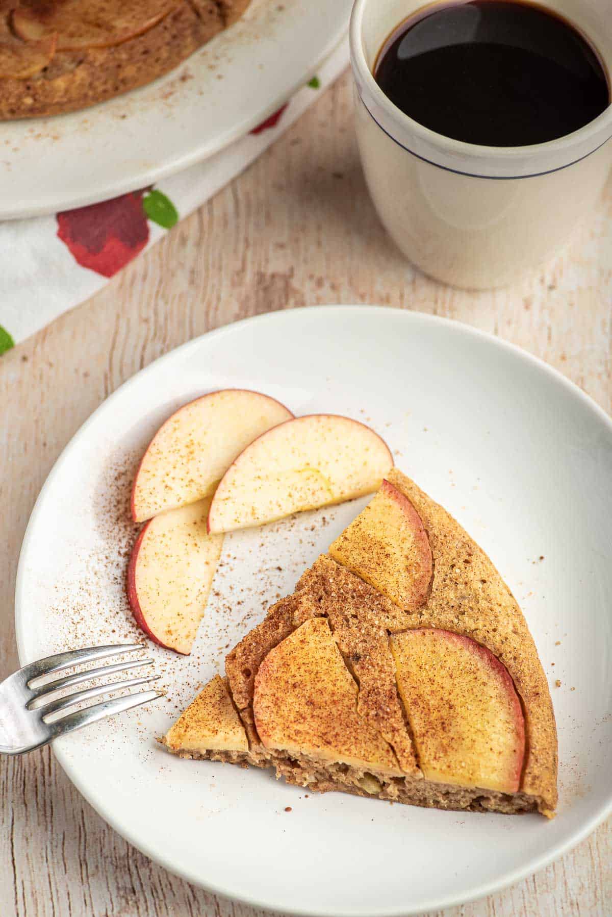 Tranche de pancake aux pommes sur un plateau blanc avec des tranches de pommes. Café en arrière-plan.