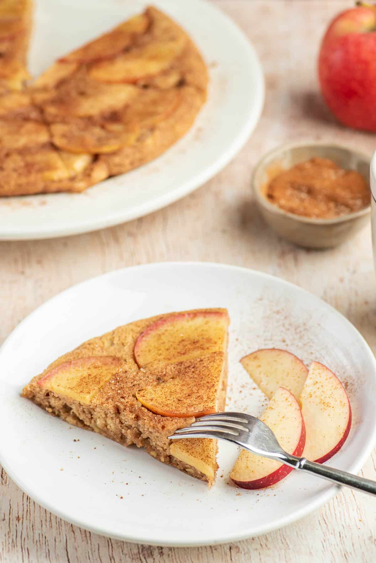 Une fourchette prenant un morceau d'un pancake aux pommes sur un plateau blanc.