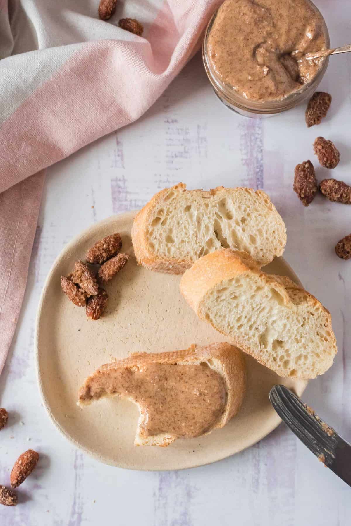 Beurre d'amande étalé sur du pain avec plus de pain et un pot de beurre d'amande à proximité.