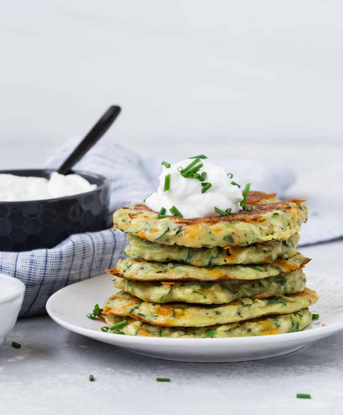Des pancakes de courgettes empilés sur une assiette blanche.