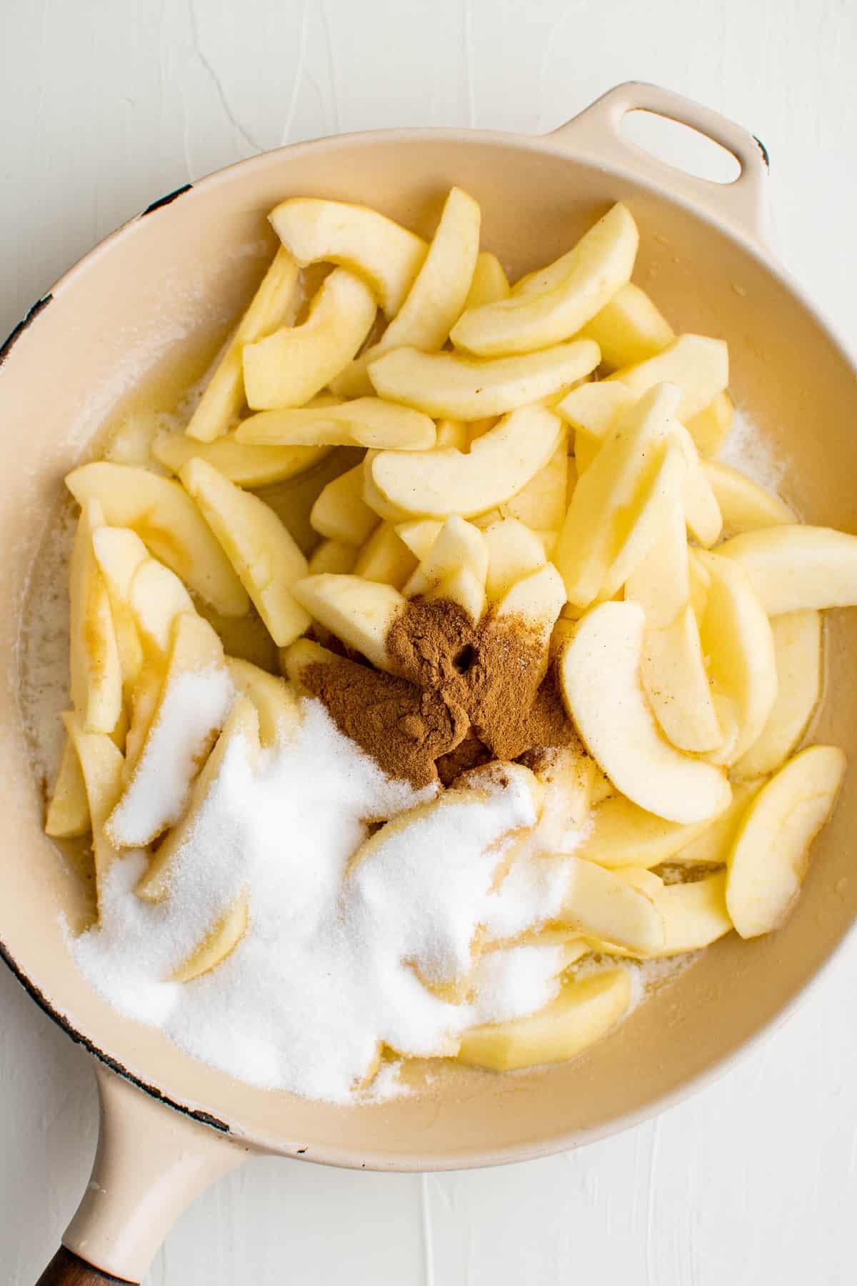 Pommes, sucre, épices et beurre dans une poêle blanche.