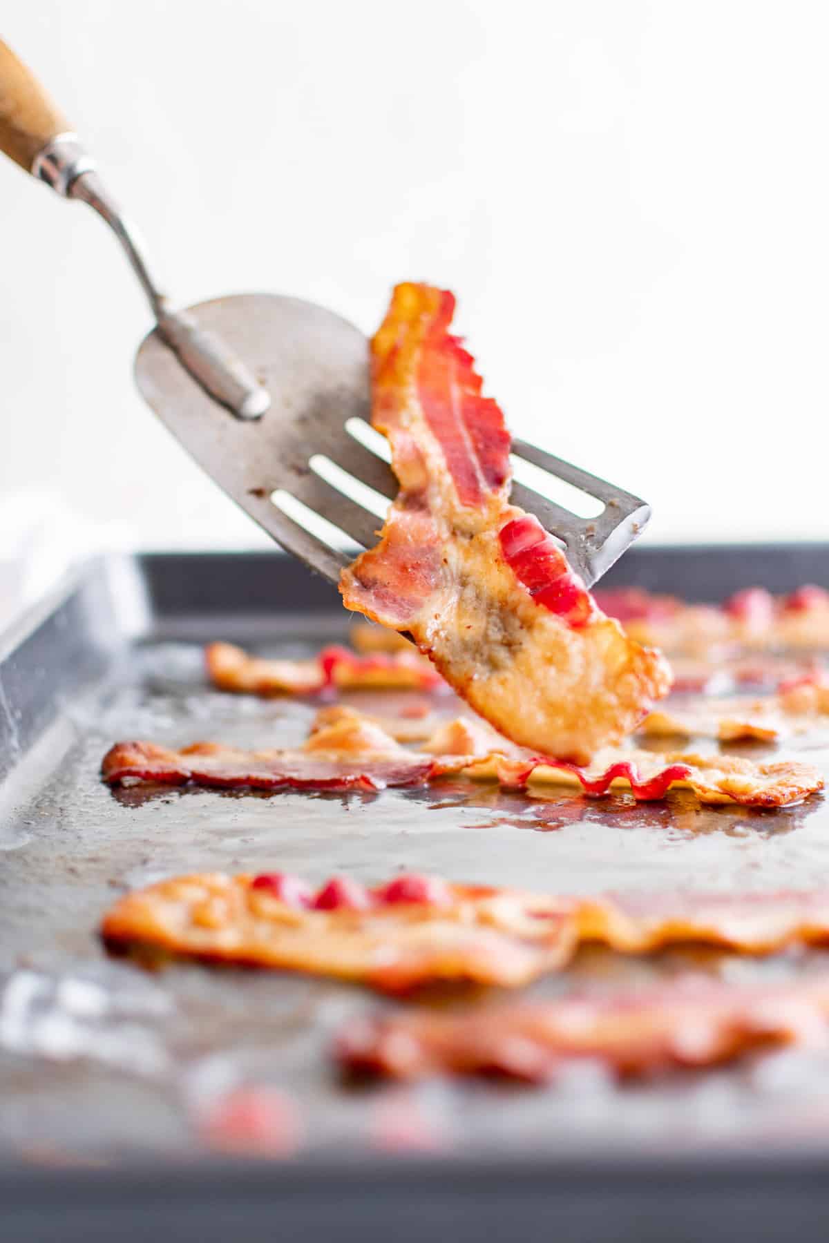 Bacon croustillant sur une spatule, plus sur une plaque à pâtisserie en arrière-plan.
