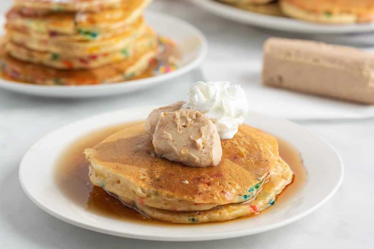 Gros plan sur le beurre de cannelle à l'érable et la crème fouettée sur une petite pile de pancakes.