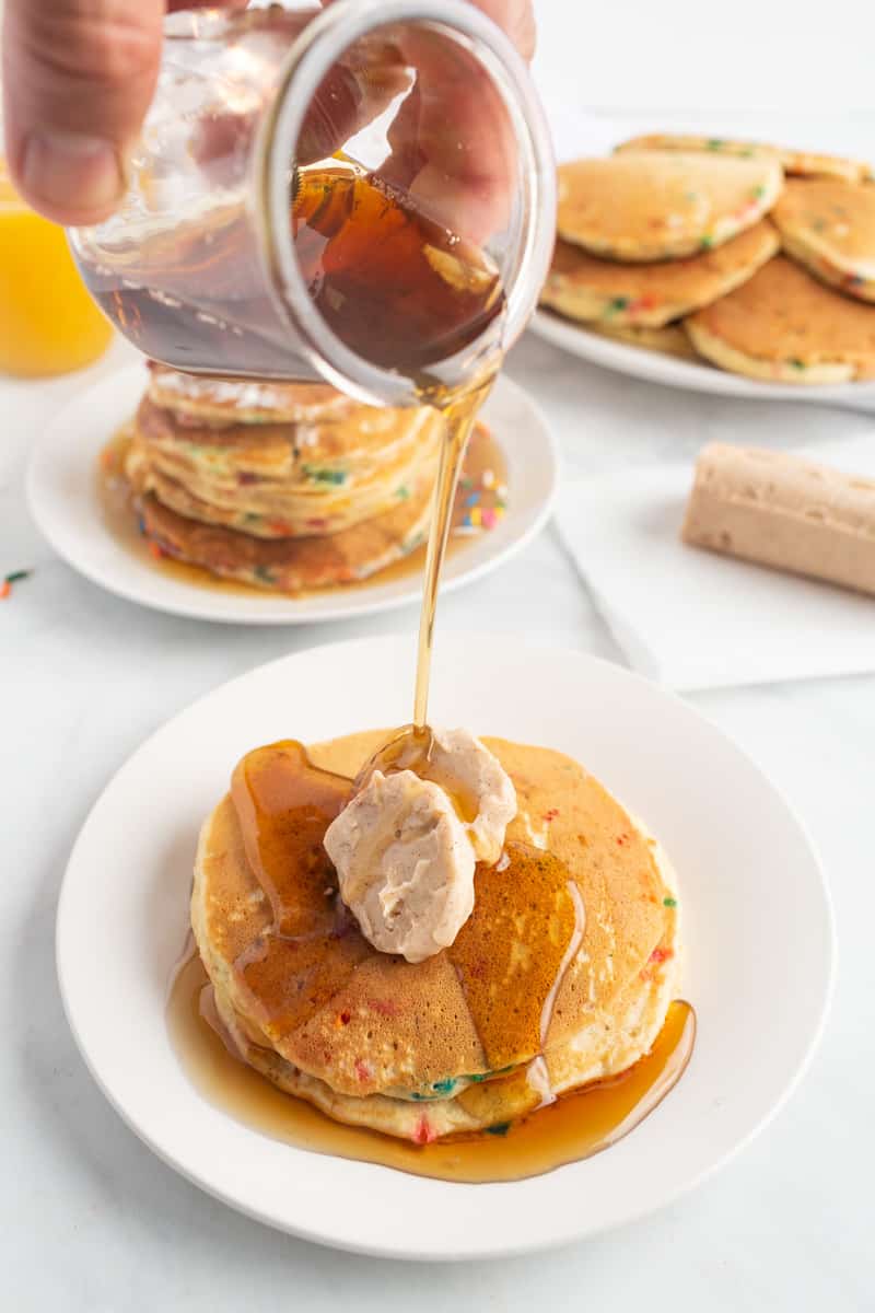 Du sirop est versé sur des pancakes garnis de deux morceaux de beurre parfumé.