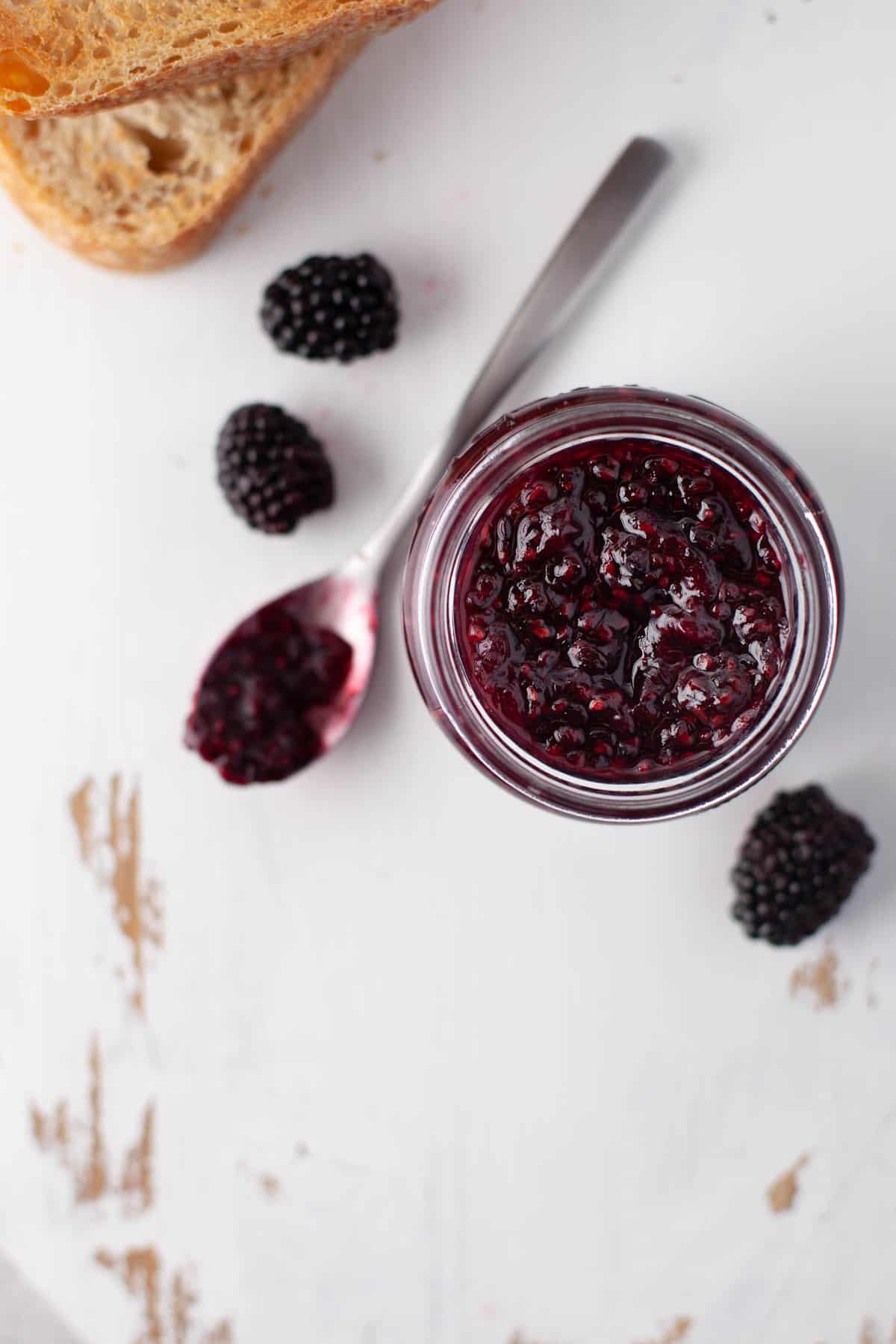 Vue de dessus d'une confiture de fruits rouges dans un pot, avec une cuillère et des mûres à côté.