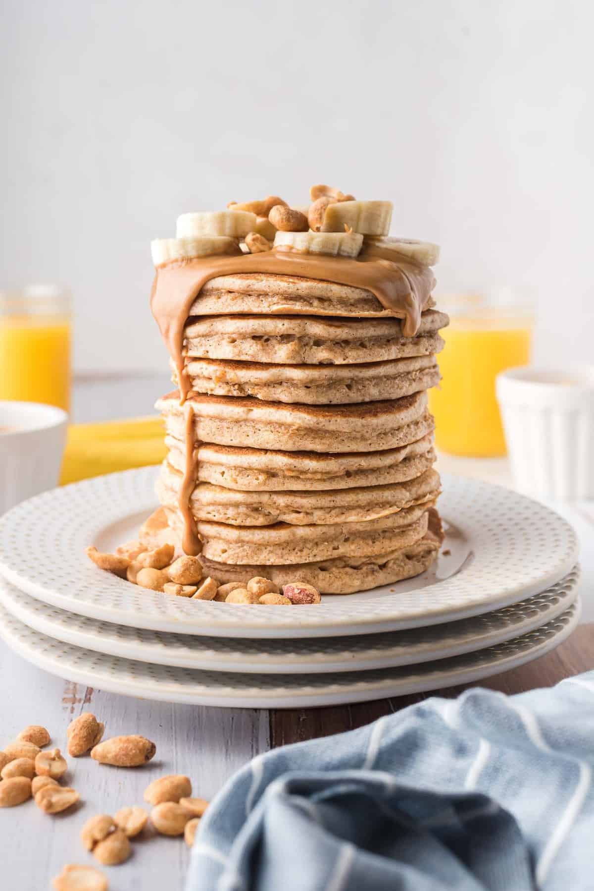 Une grande pile de pancakes dégoulinants de beurre de cacahuète et garnis de tranches de banane.
