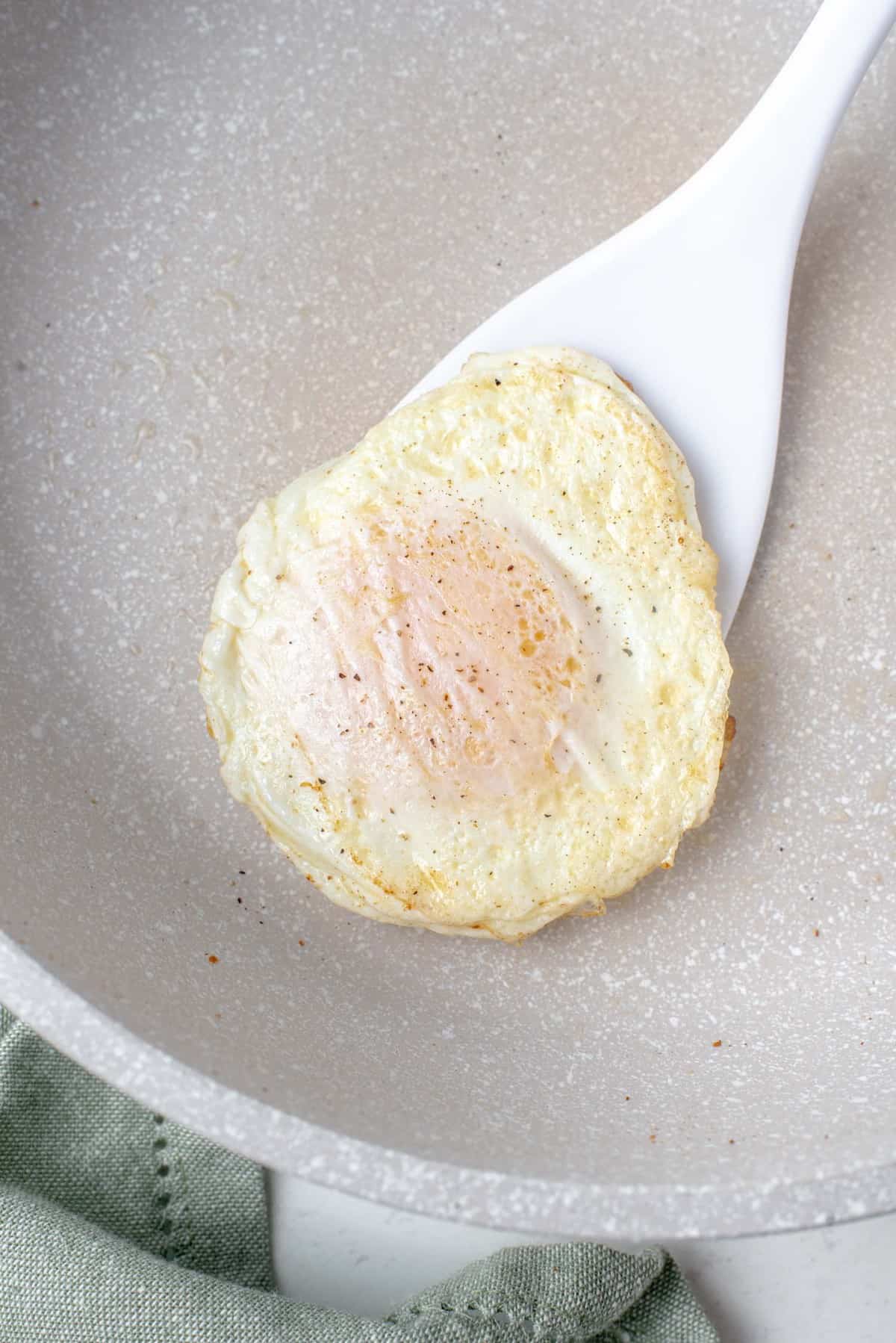Un œuf en train d'être retourné avec une spatule blanche.
