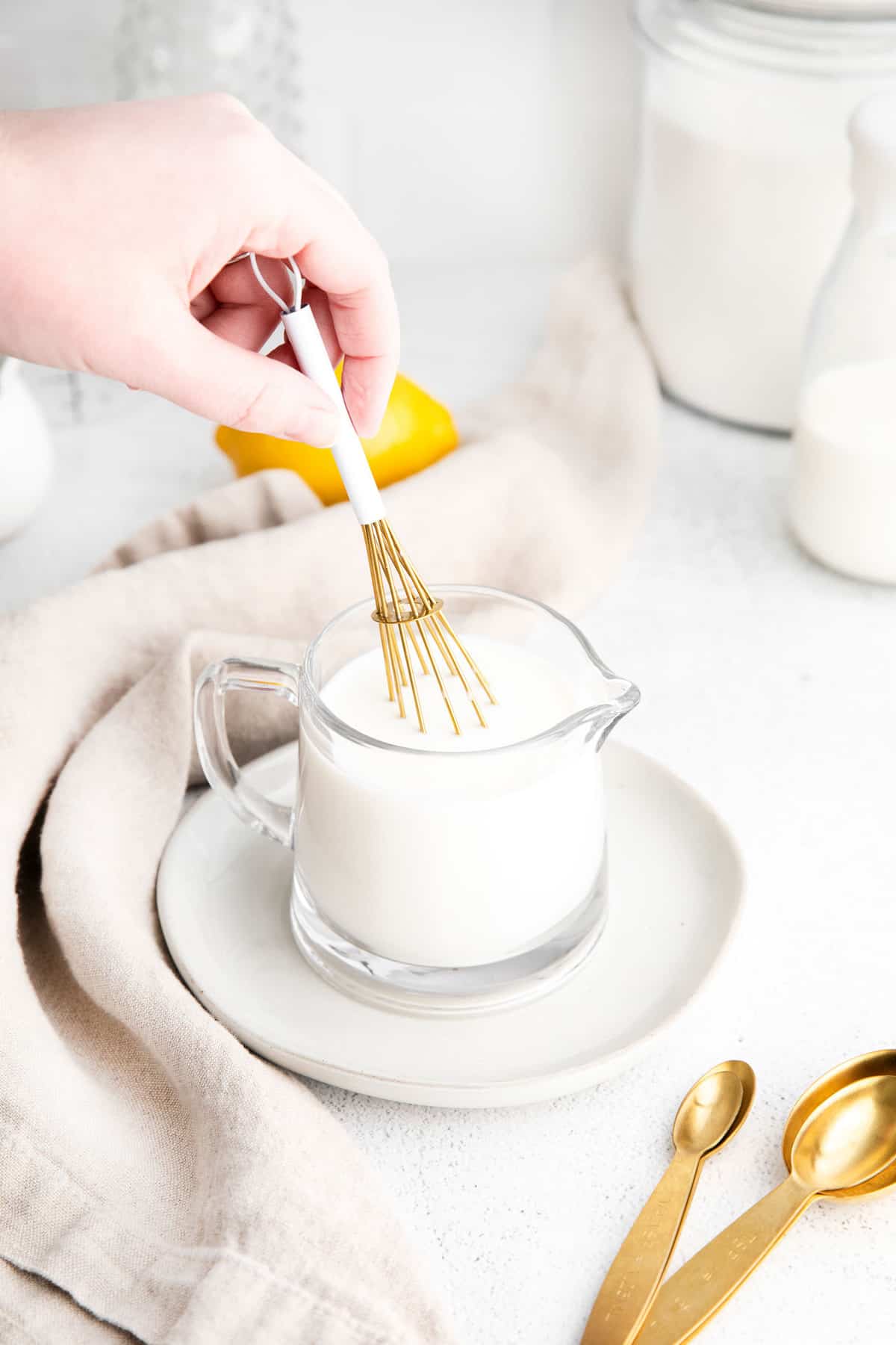 Petit pichet en verre de lait, avec une main remuant avec un petit fouet.