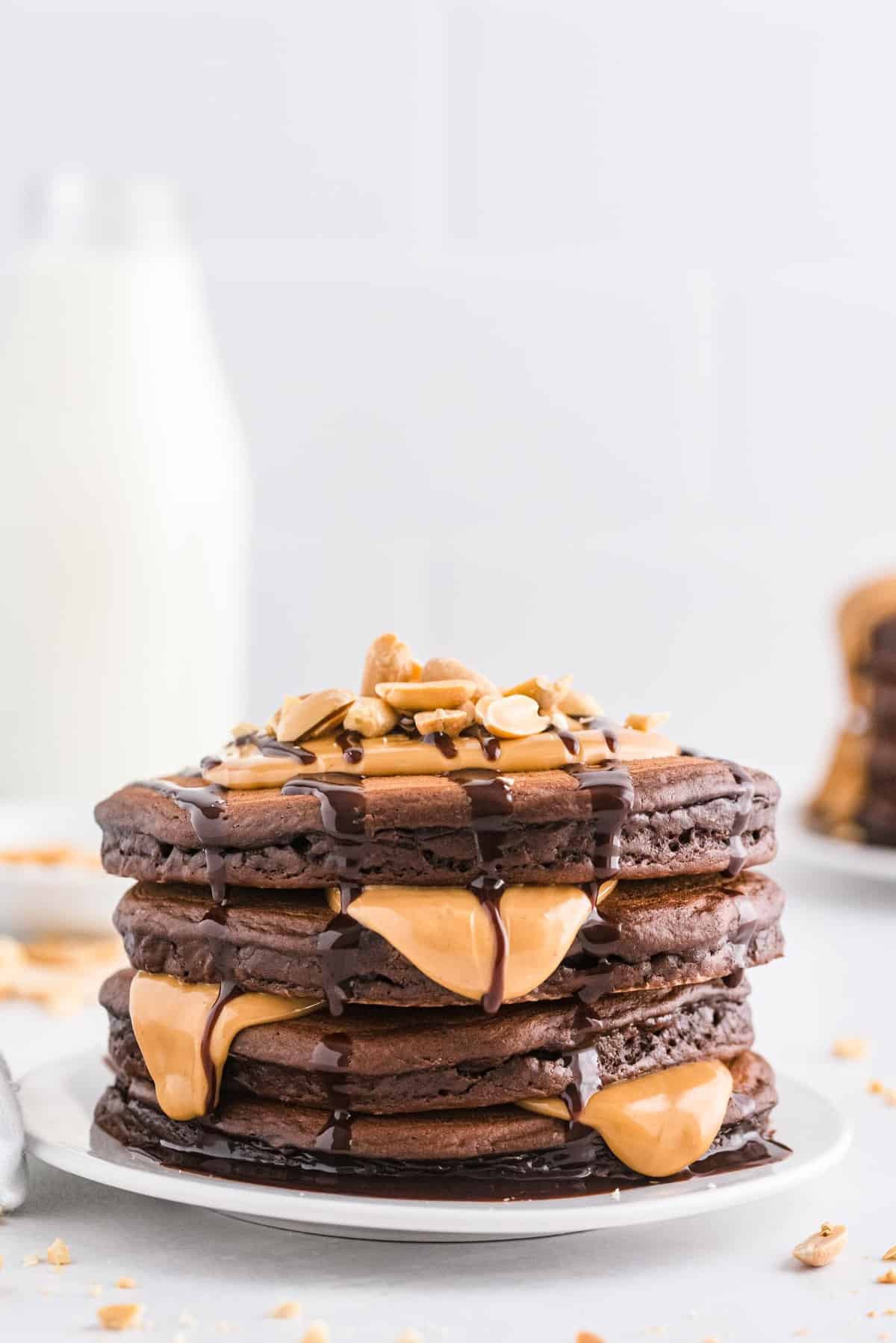 Empilement de pancakes dégoulinant de sirop de chocolat et de beurre de cacahuète fondu.